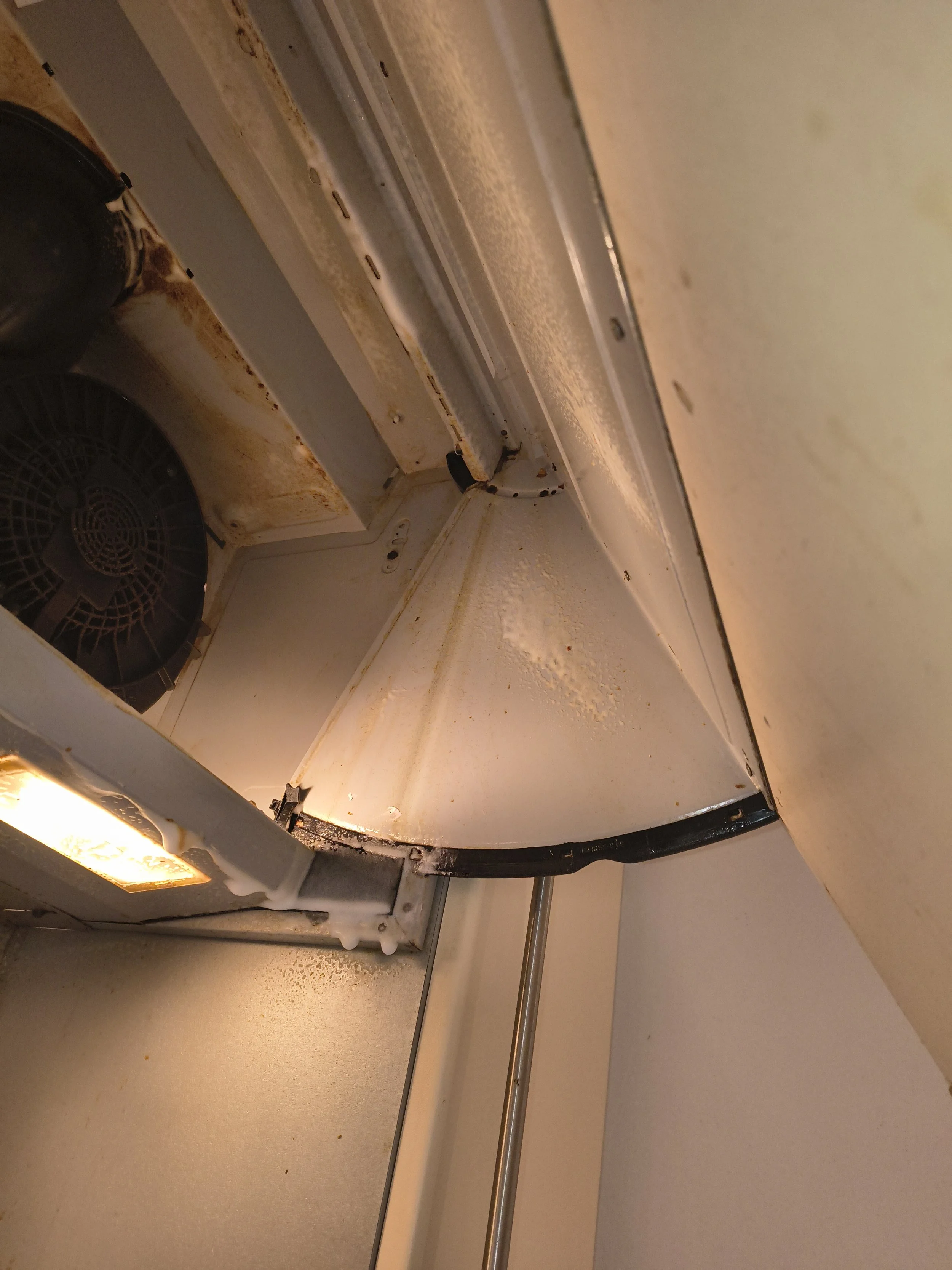The interior of an old, rusty microwave oven with visible rust spots and dirt, showing the inside chamber and a fan on the side.