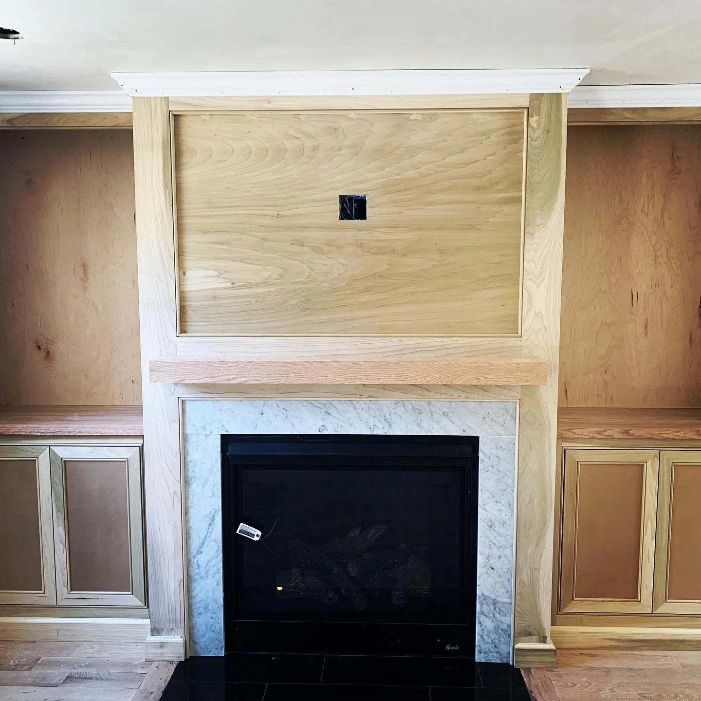 Image of a built-in wooden fireplace with cabinetry on either side, a marble surround, and a wooden panel above the fireplace with an electrical outlet.