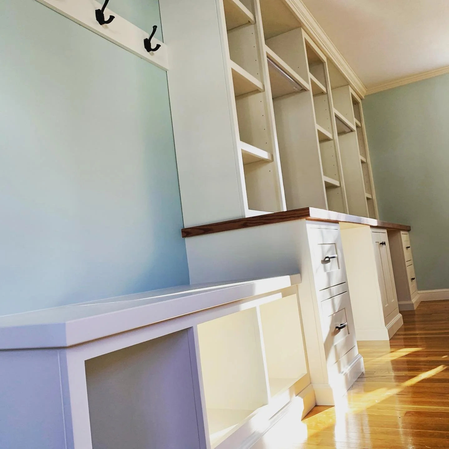 Empty white built-in shelves and cabinets in a room with light blue walls and wooden flooring.