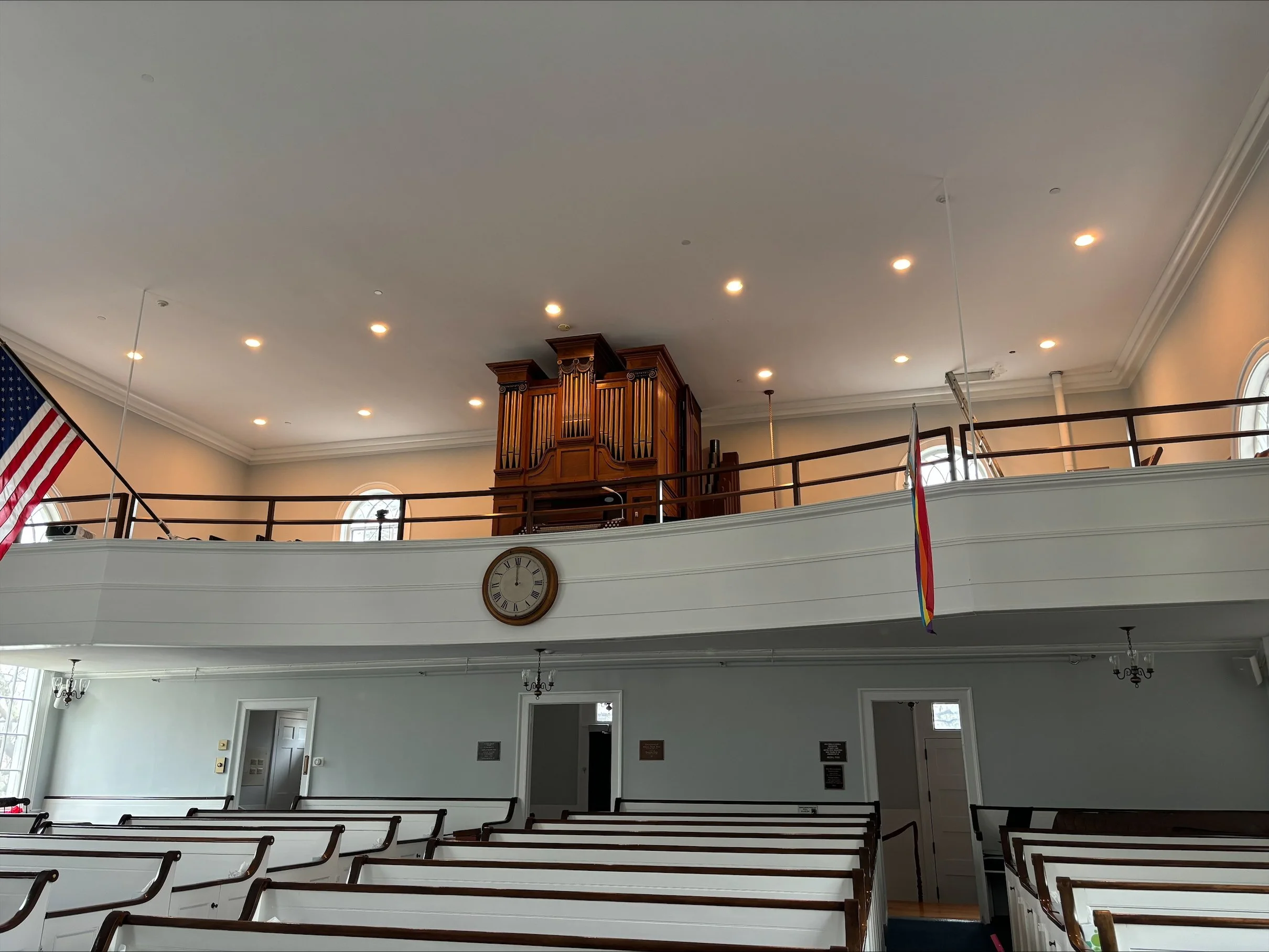 Interior of a church or chapel with pews, a clock, an organ, and flags.