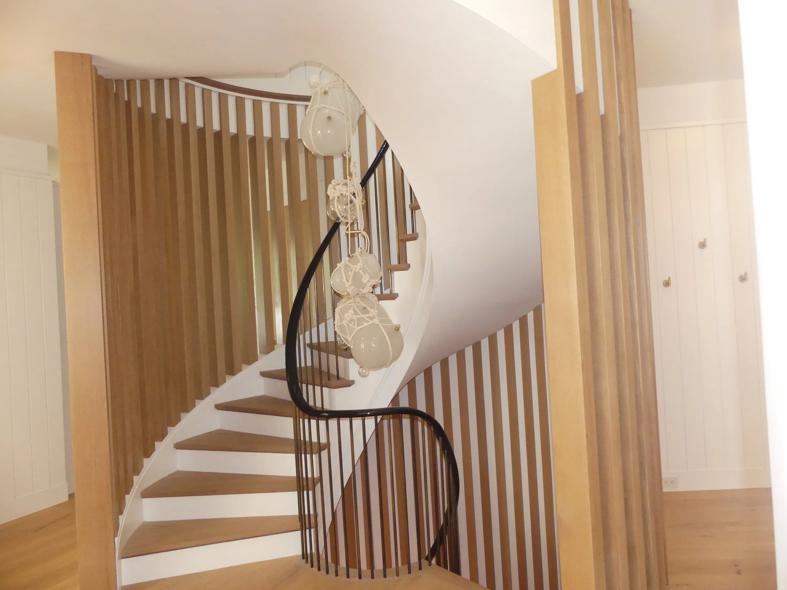 Spiral staircase with wooden steps, black railing, and hanging spherical light fixtures in a modern home interior.