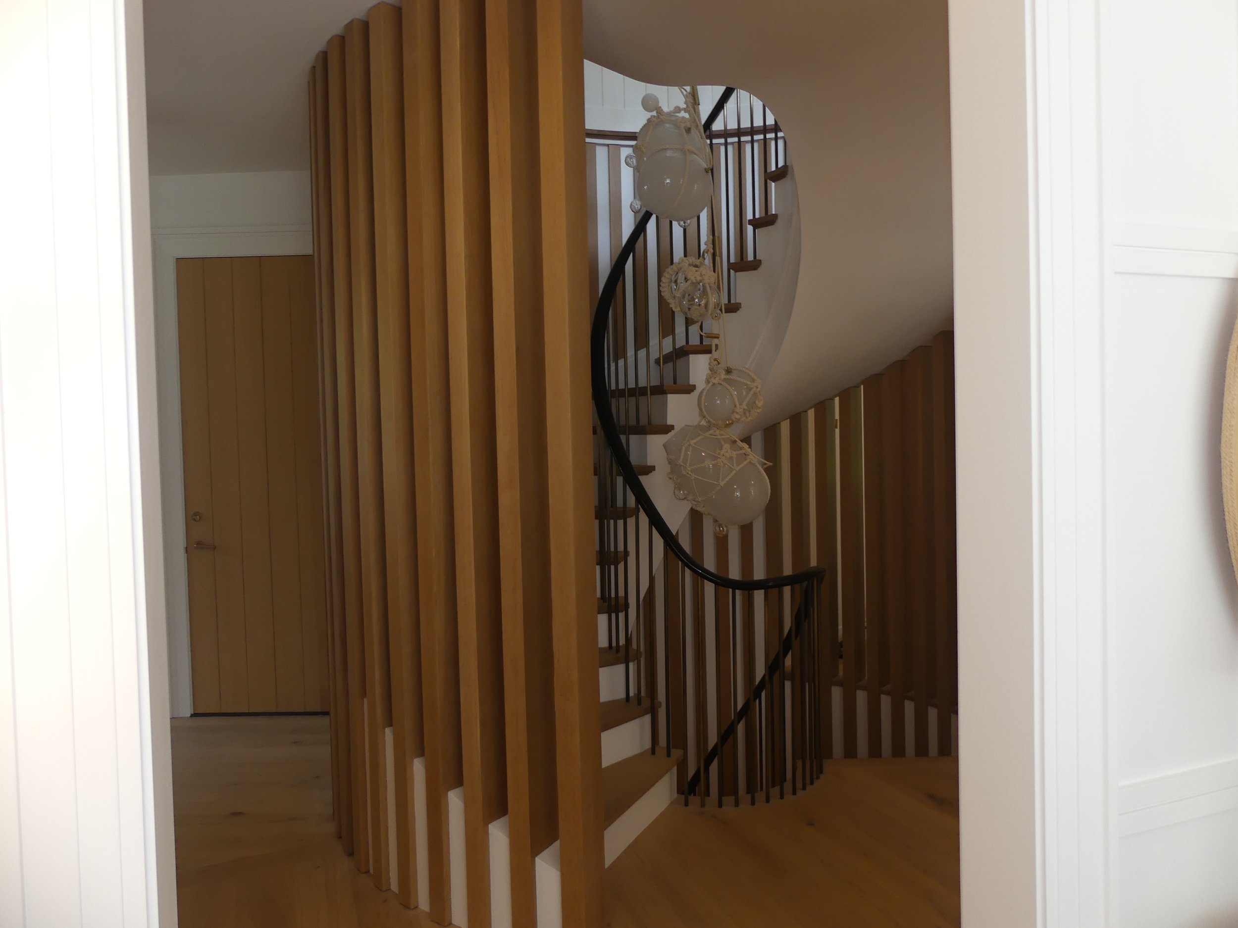 Spiral staircase with wooden steps and black railing, decorated with hanging glass pendant lights, in a modern interior with wood and white walls.