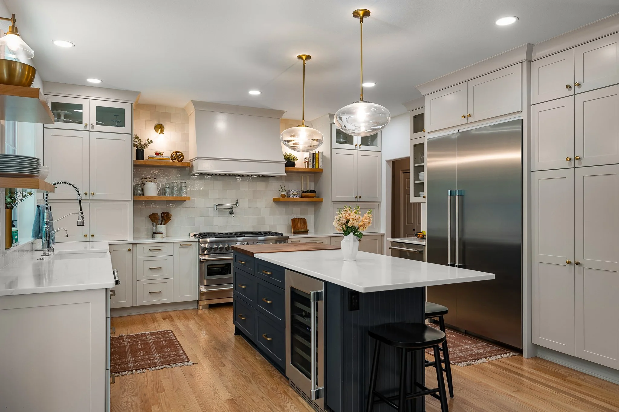 Modern kitchen with white cabinets, a central island with a dark blue base, a white countertop, and two glass pendant lights hanging from the ceiling.