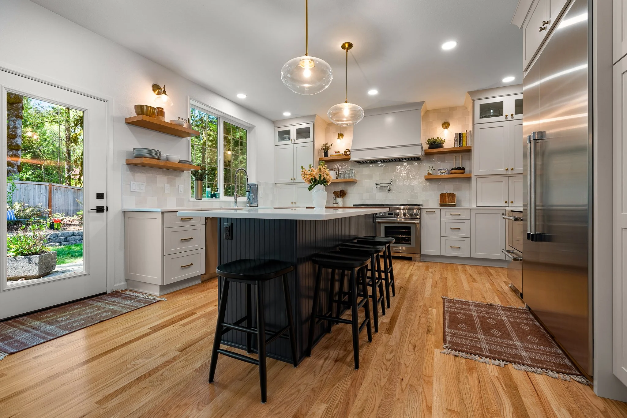 Modern kitchen with white cabinets, black island with barstools, stainless steel appliances, wood accents, and hardwood floors.
