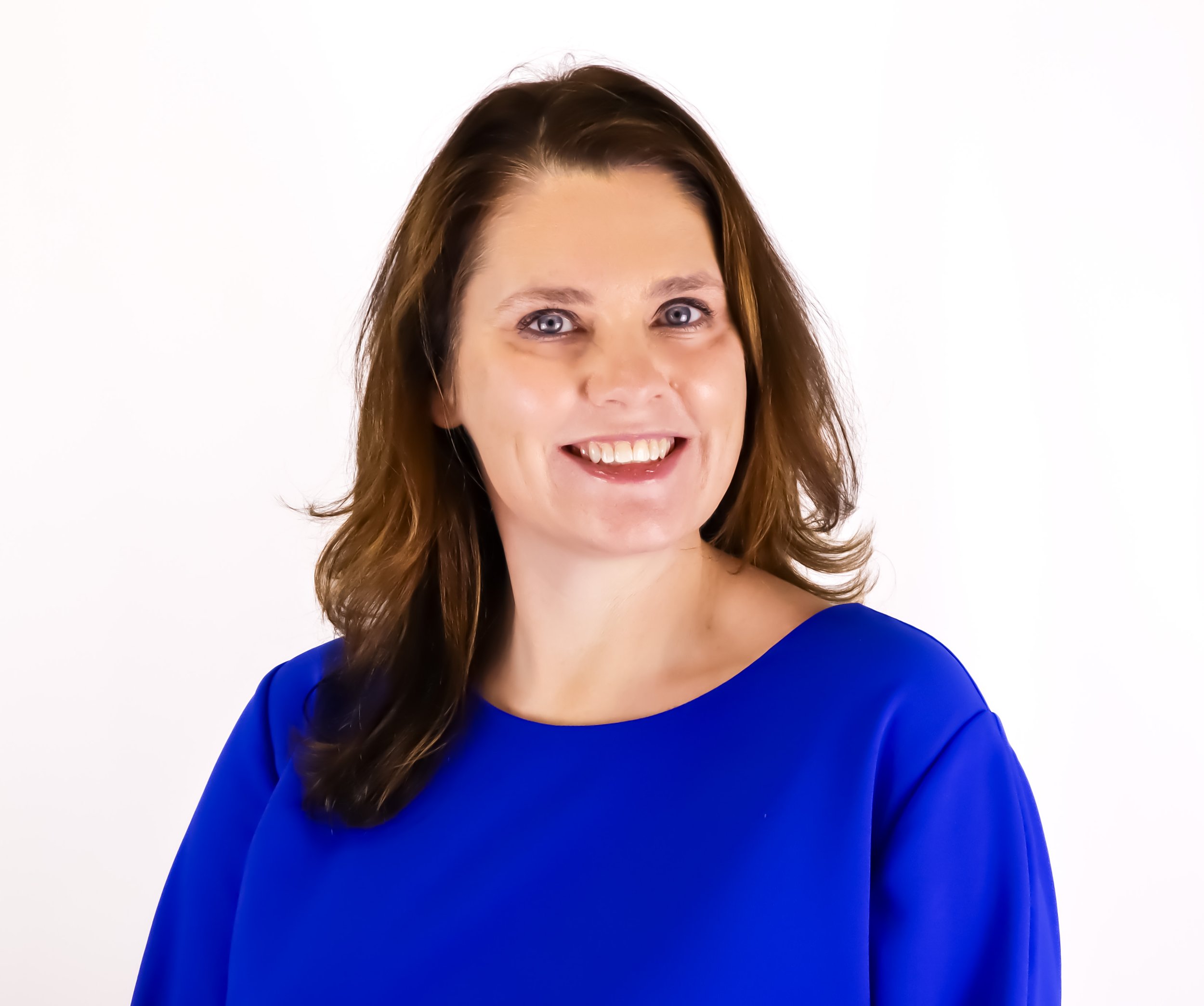 Smiling woman with shoulder-length brown hair and blue eyes, wearing a royal blue blouse, against a white background.
