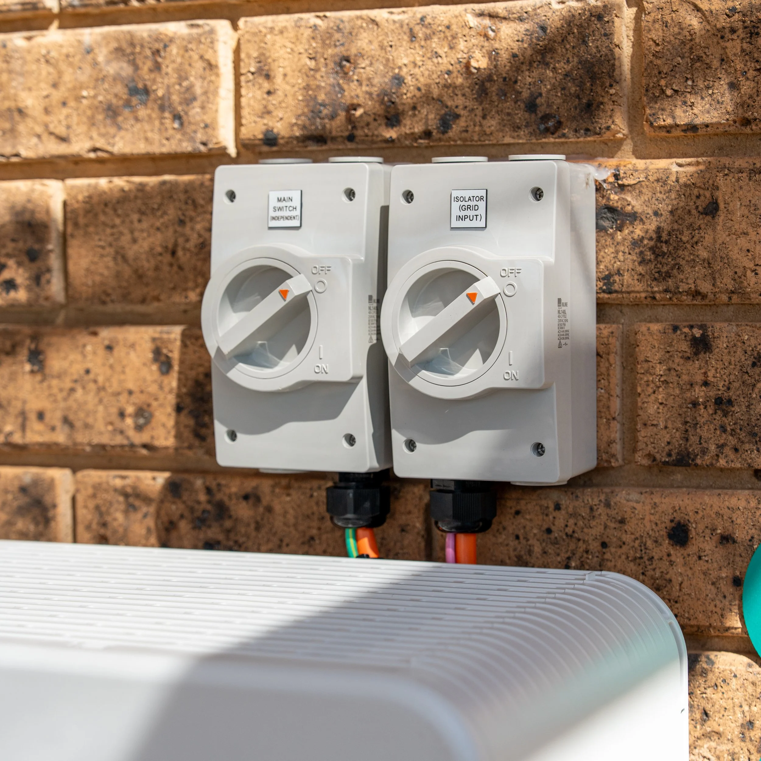 Electrical power outlets mounted on a brick wall, with two switches labeled 'Main Switch' and 'Isolator Grid Input'.
