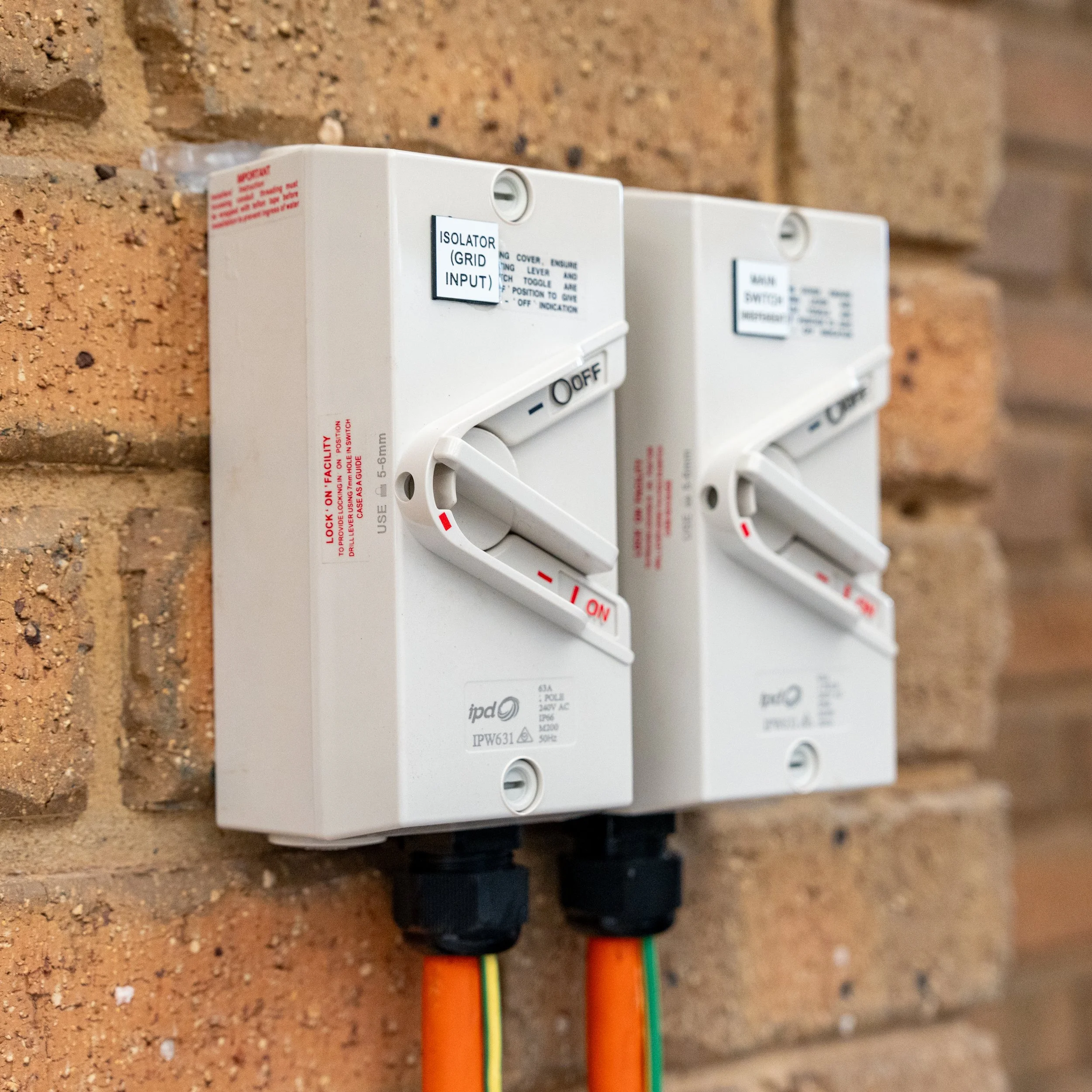 Two electrical switches mounted on a brick wall with orange, green, and yellow wires connected at the bottom Solar Batteries