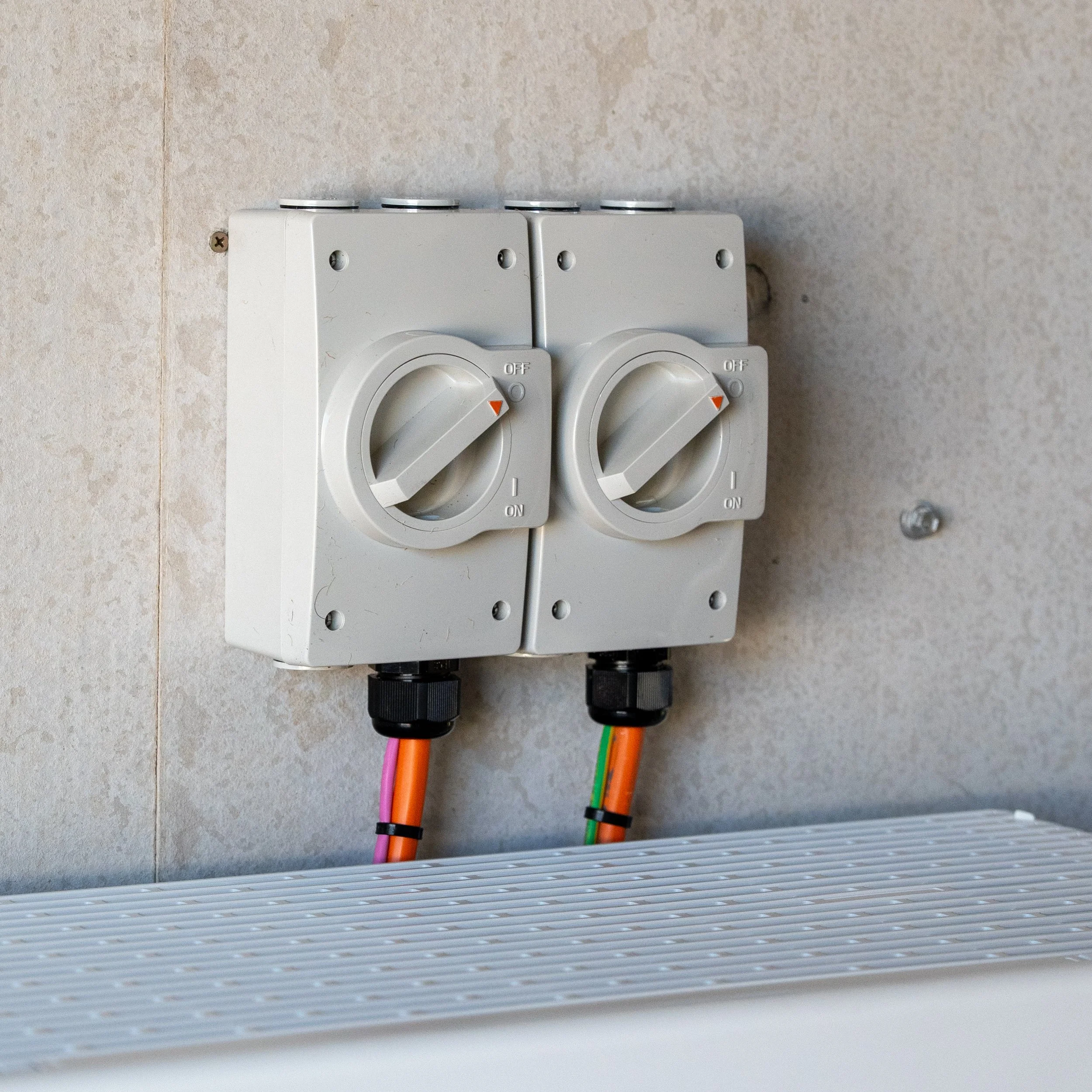Electrical outlets with switches on a wall with colorful wiring connected to the outlets.