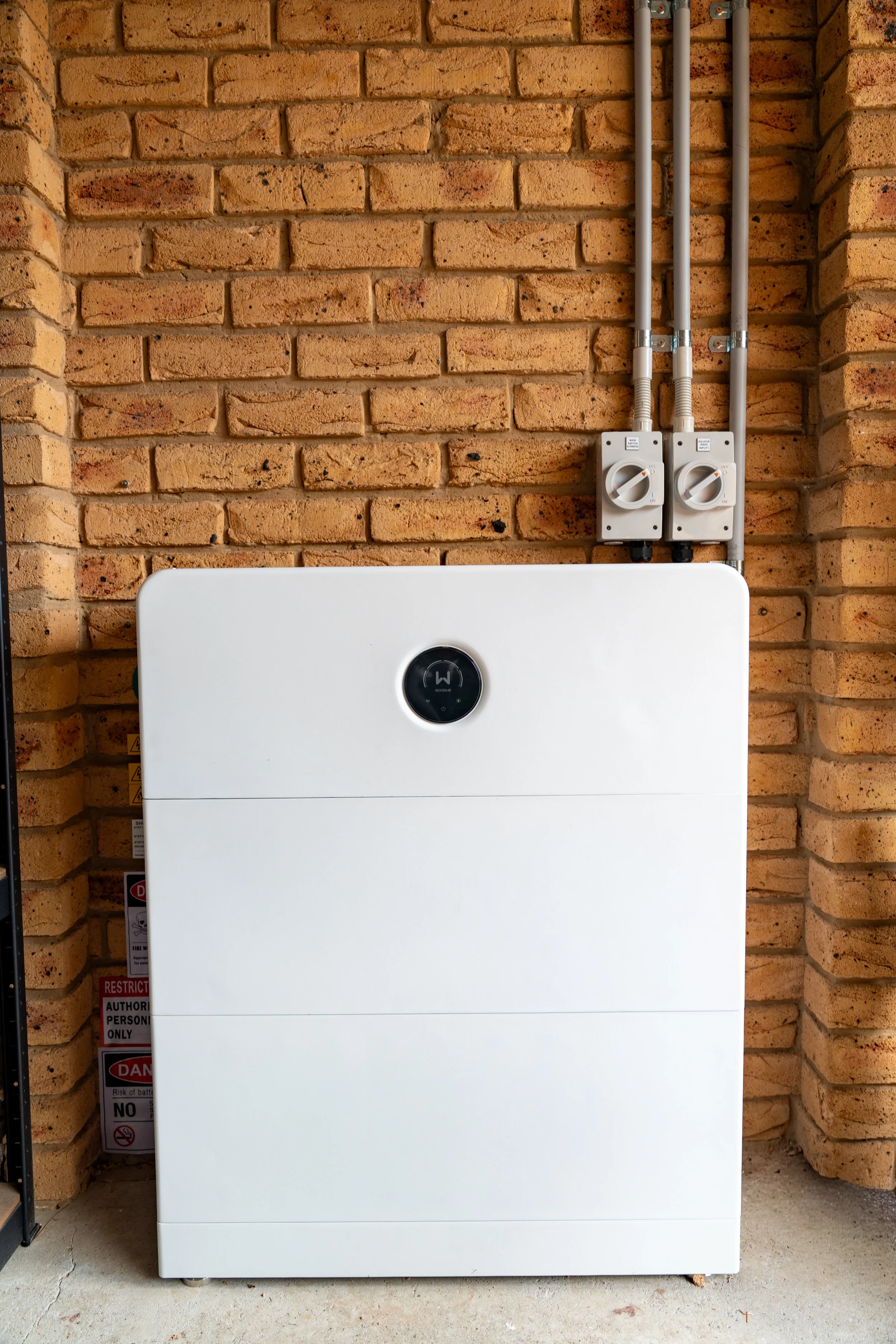 Residential solar battery storage system installed on exterior brick wall for storing excess solar energy from rooftop panels.