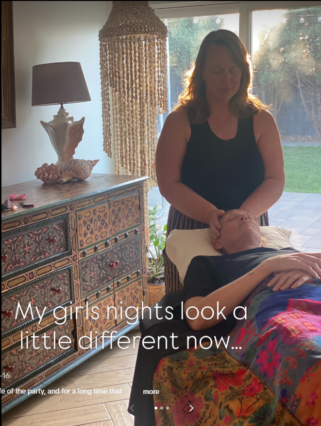 A woman giving a facial massage to a person lying on a massage table in a sunlit room with a large window and decorative decor.