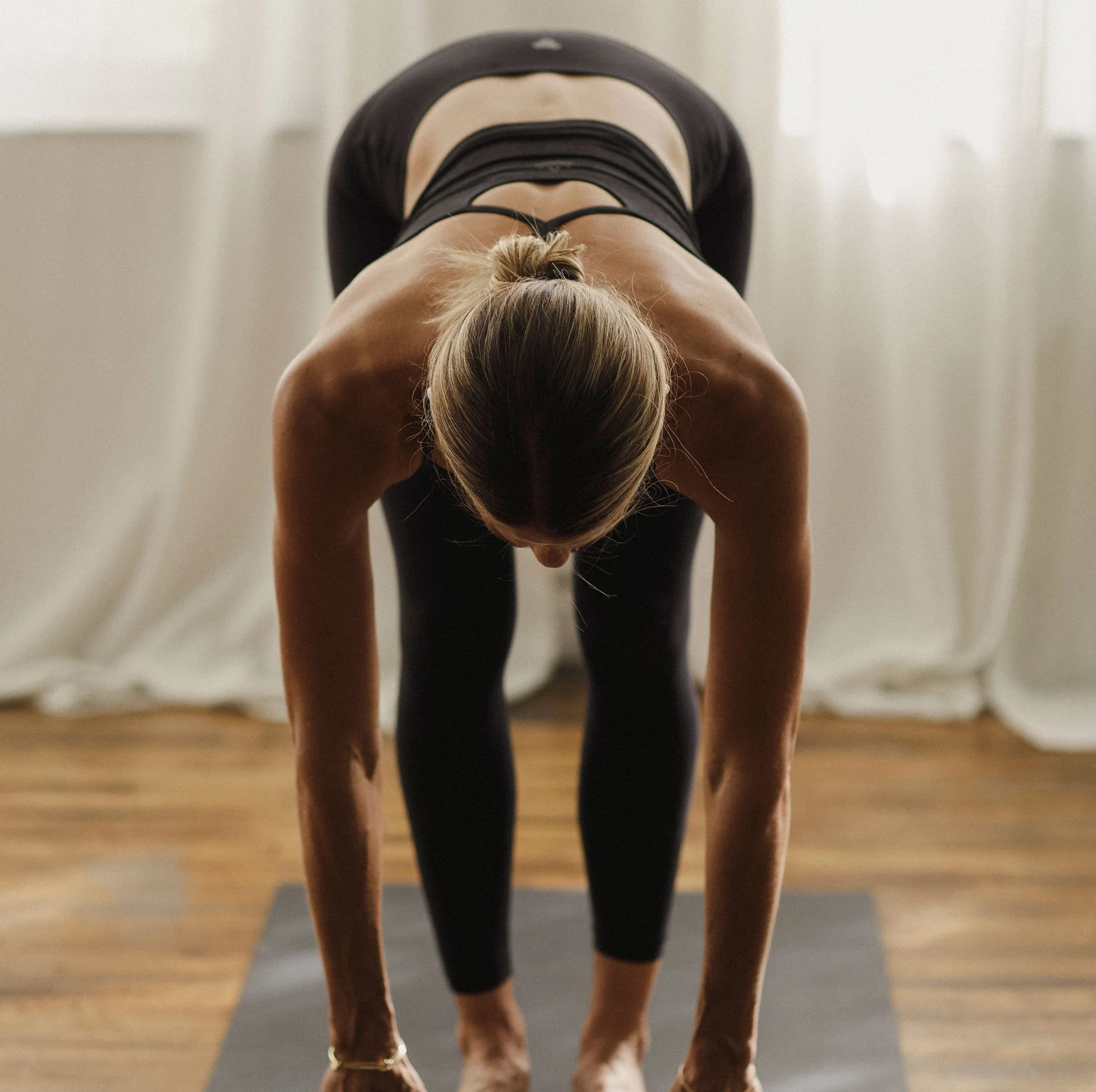 Multiple horses' legs and bodies, shown from a low angle, with a person doing yoga on the floor in the background.