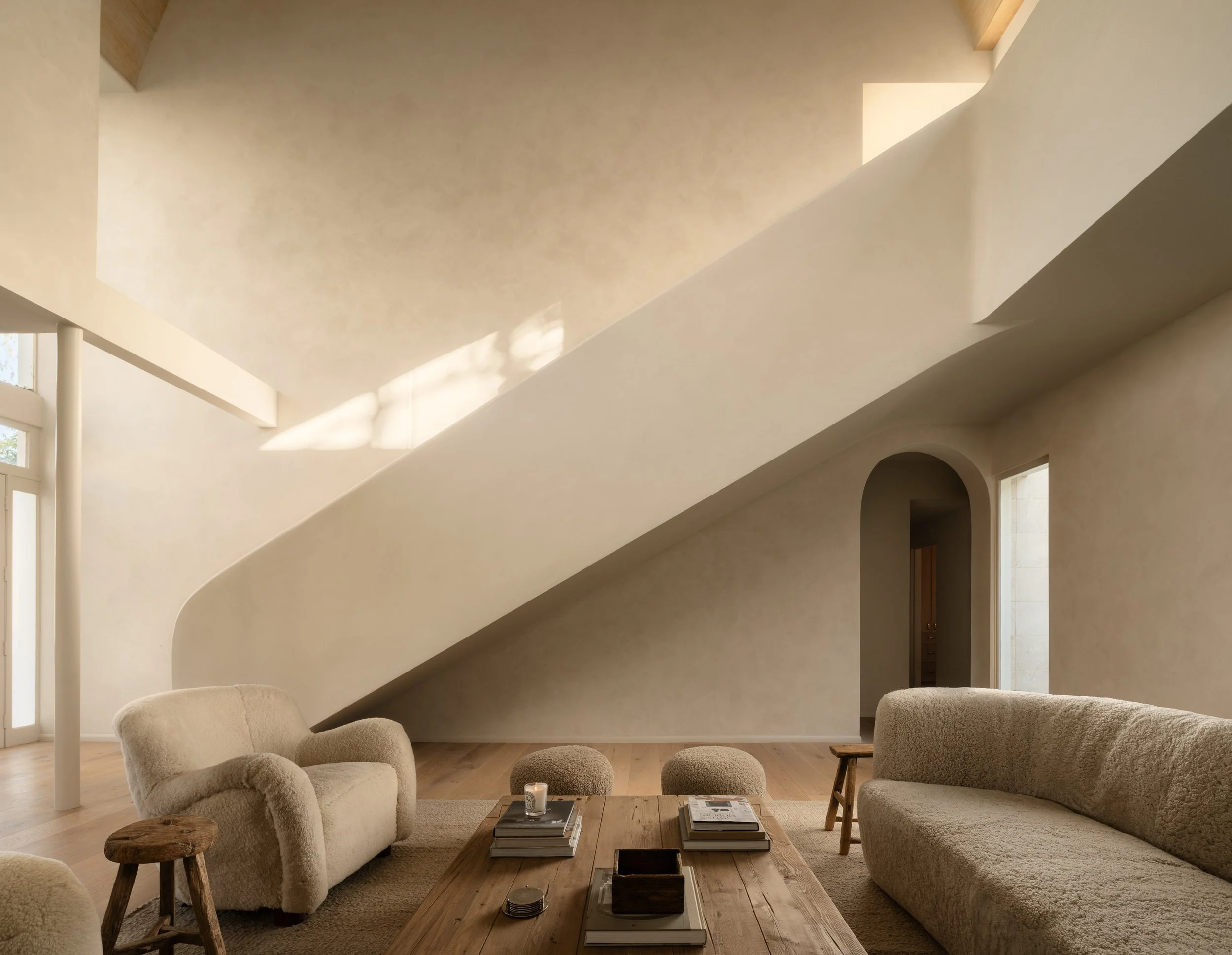 Double-height living room with sculptural staircase, limewashed walls, and warm contemporary furnishings, completed by JBurton General Contractor for a luxury home remodel in Benedict Canyon, Los Angeles.