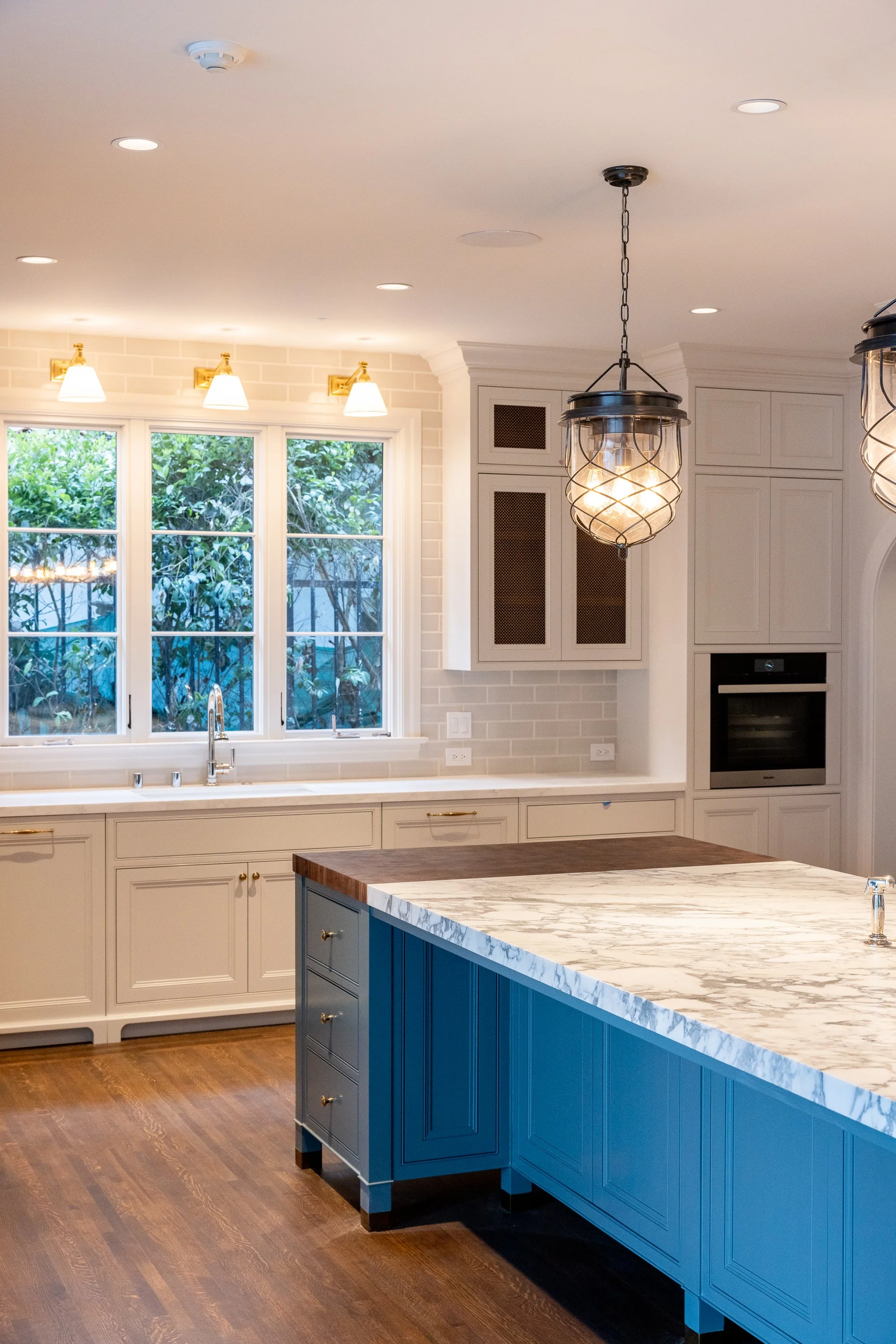 Bright custom kitchen with marble countertops, blue island, and traditional lighting, remodeled by JBurton General Contractor in Hancock Park, Los Angeles.