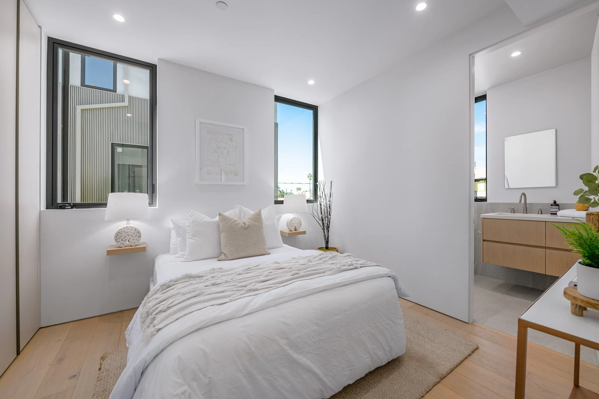 Comfortable secondary bedroom featuring oversized windows, warm wood flooring, and bright contemporary finishes by JBurton General Contractor.