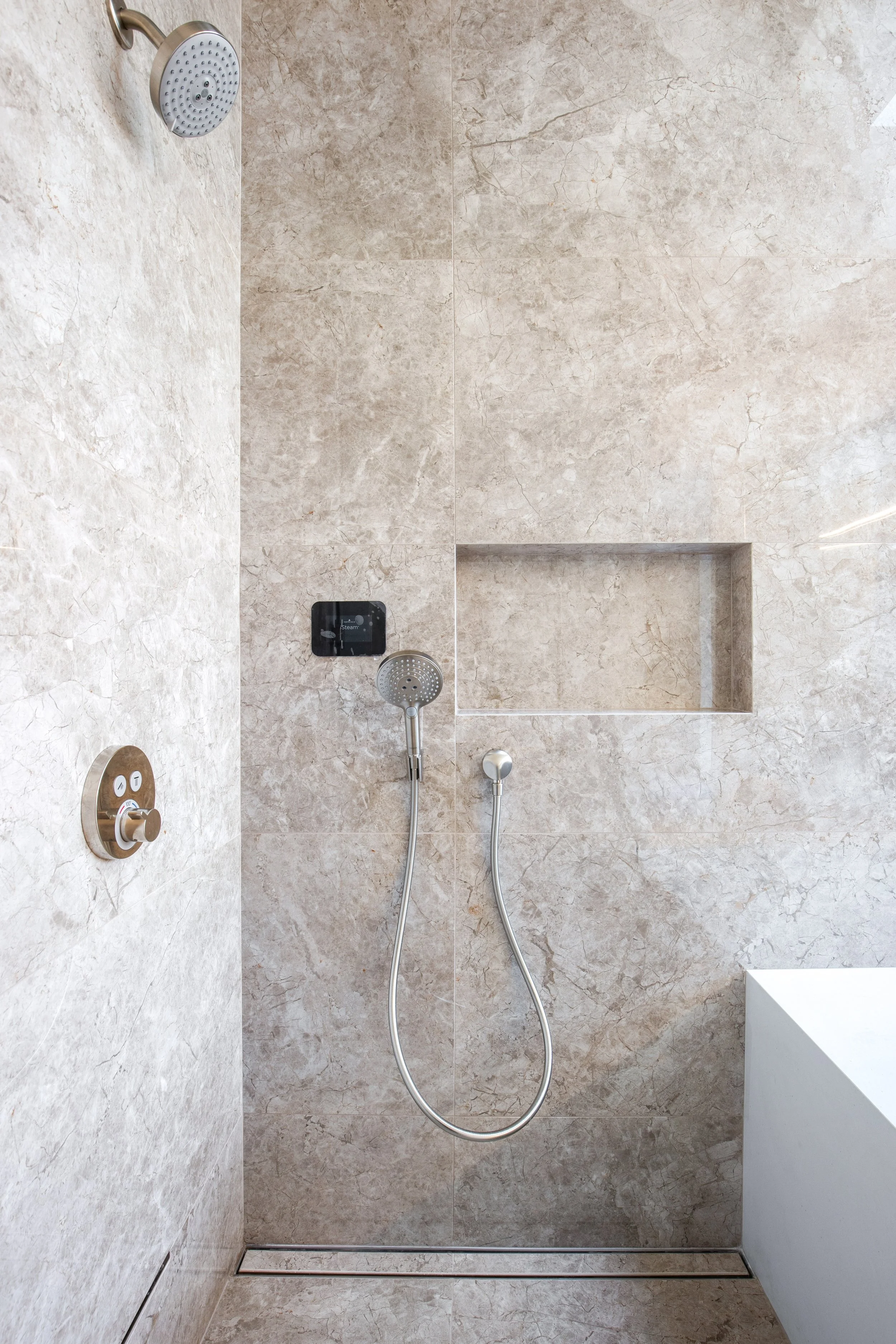 Spa-inspired shower featuring large-format natural stone tile and recessed shower niche by JBurton General Contractor.