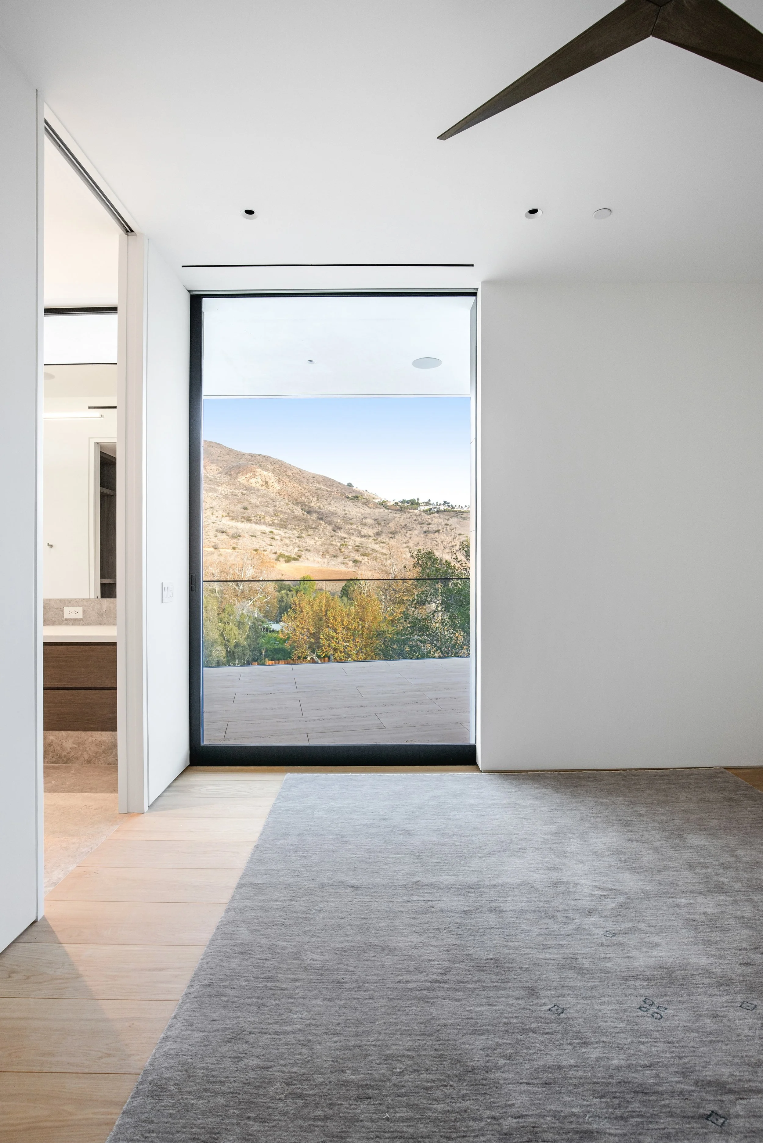 Bedroom with floor-to-ceiling glazing framing panoramic mountain views in a custom Malibu home by JBurton General Contractor.