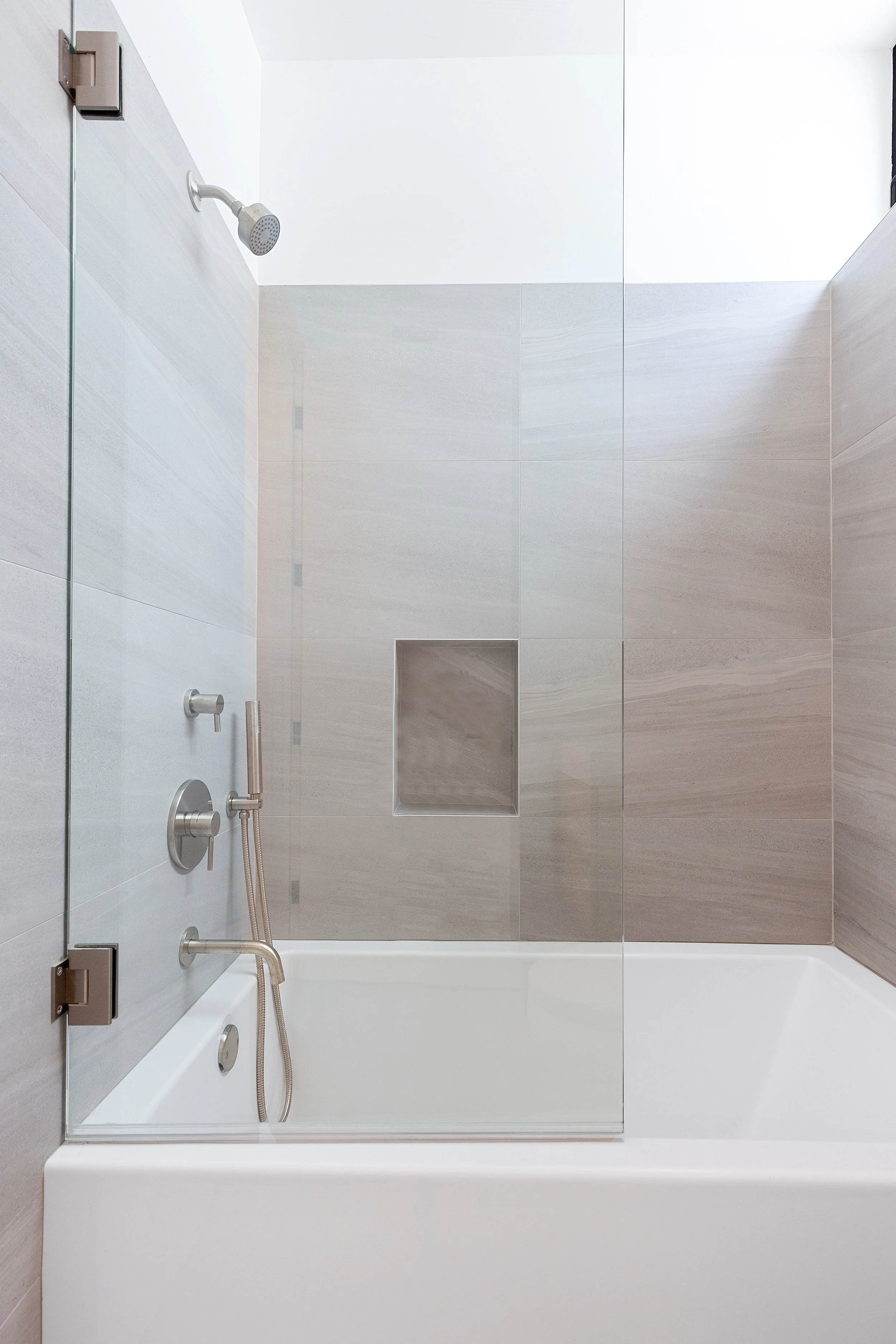 Contemporary bathroom with a glass-enclosed tub and shower, porcelain tile walls, and recessed niche, built by JBurton General Contractor in Faircrest Heights.