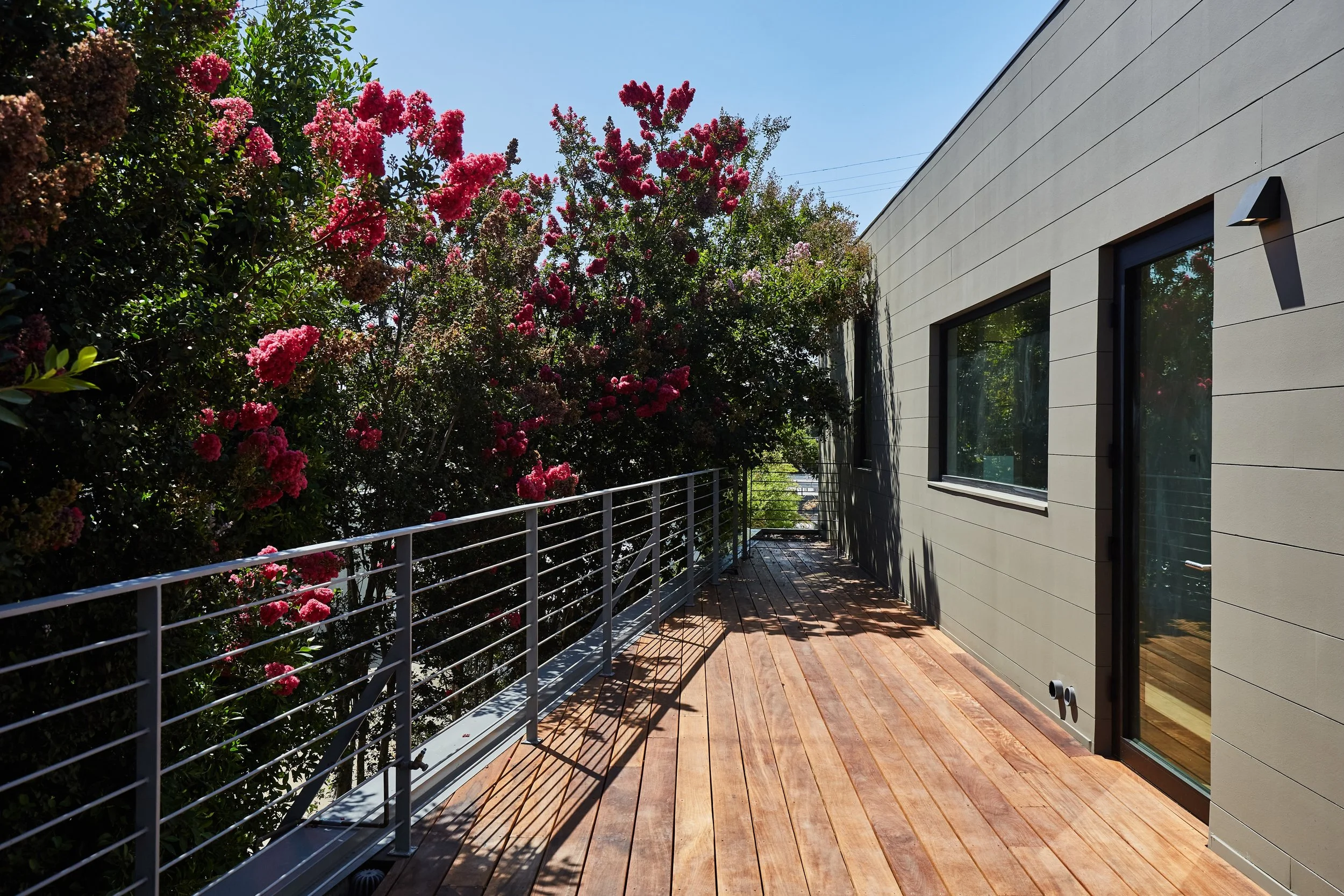 Private outdoor deck with contemporary steel railings, warm wood decking, and landscaped privacy, creating an inviting extension of the home by JBurton General Contractor.