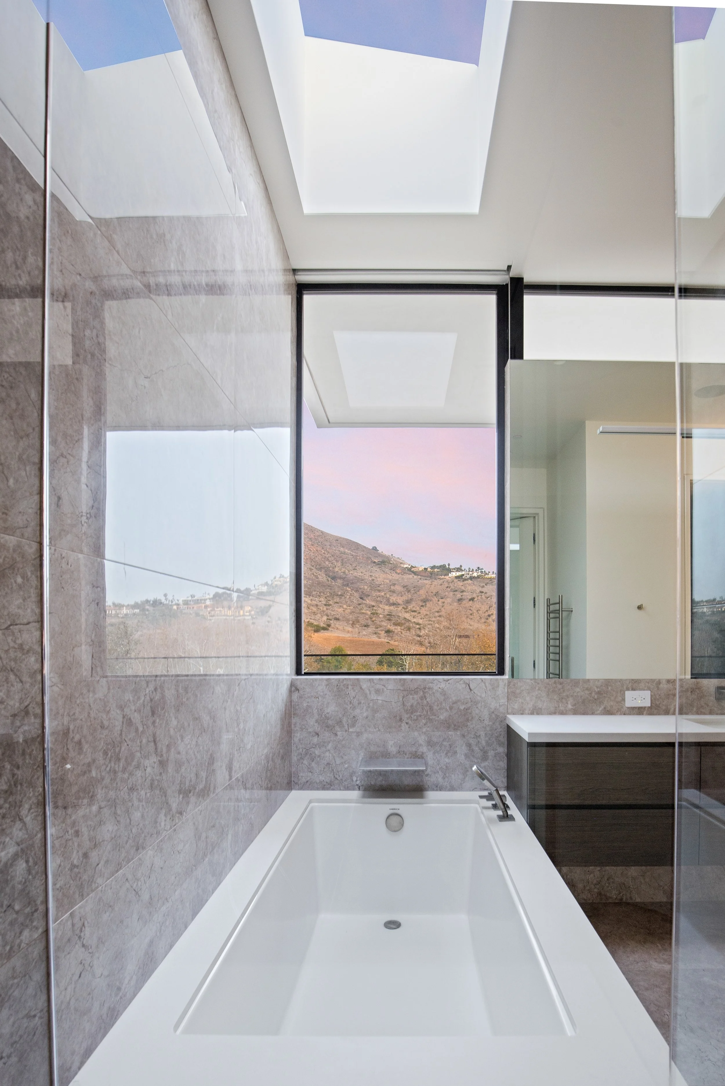 Spa-inspired primary bathroom featuring a freestanding soaking tub, natural stone finishes, and panoramic mountain views, crafted by JBurton General Contractor.