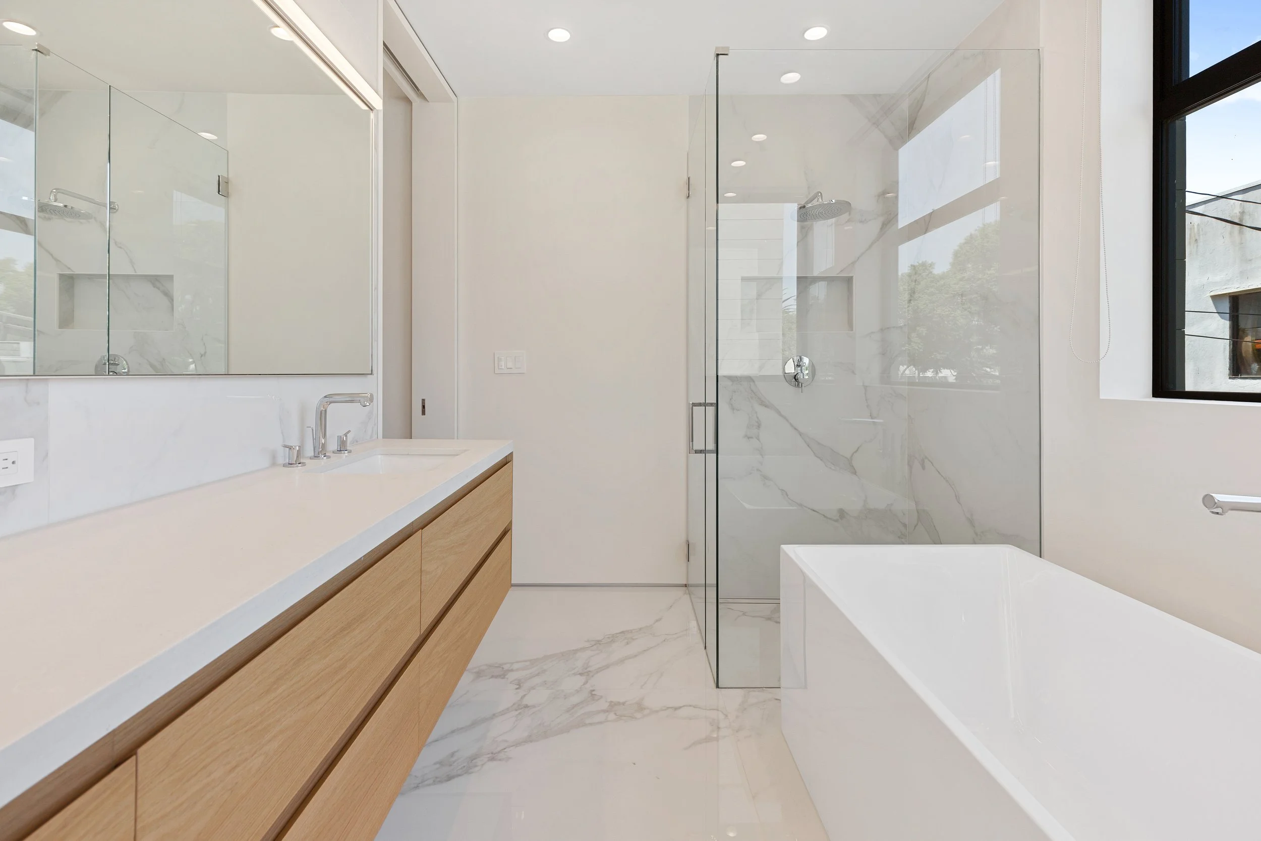 Spa-inspired primary bathroom featuring a floating vanity, freestanding soaking tub, oversized walk-in shower, and elegant marble finishes by JBurton General Contractor.