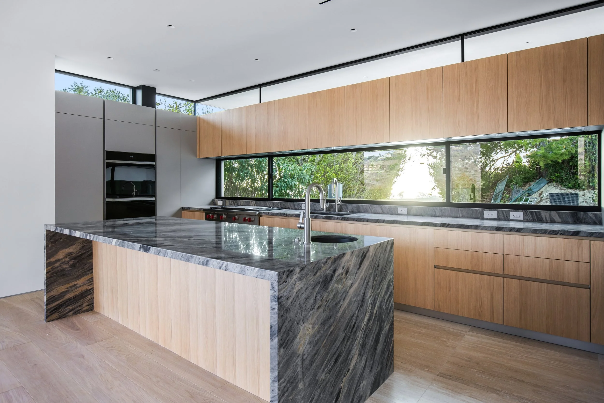Luxury Malibu kitchen with a contrast stone waterfall island, expansive windows, and custom millwork by JBurton General Contractor.