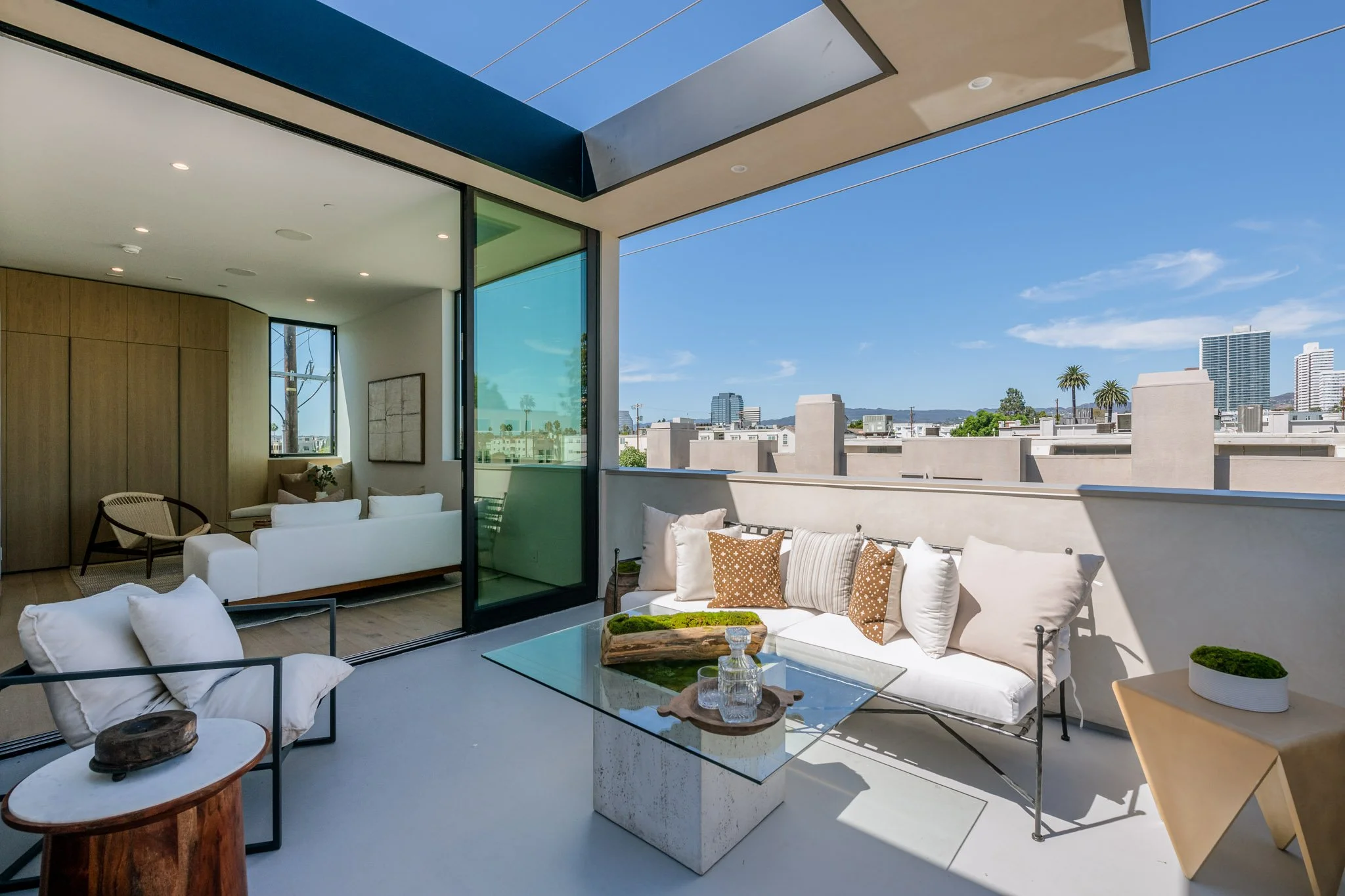 Covered outdoor lounge extending from the living area, featuring comfortable seating, a skylight, and city views, designed and built by JBurton General Contractor.