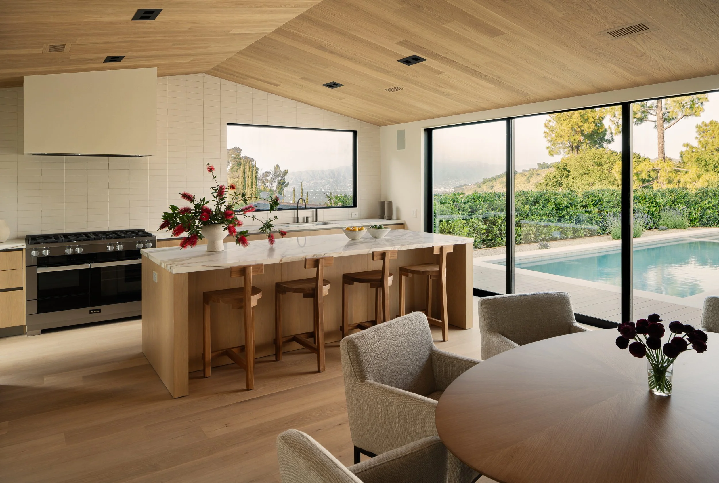 Custom kitchen with a waterfall island, wood cabinetry, and panoramic indoor-outdoor views, remodeled by JBurton General Contractor in Beverly Crest, Los Angeles.