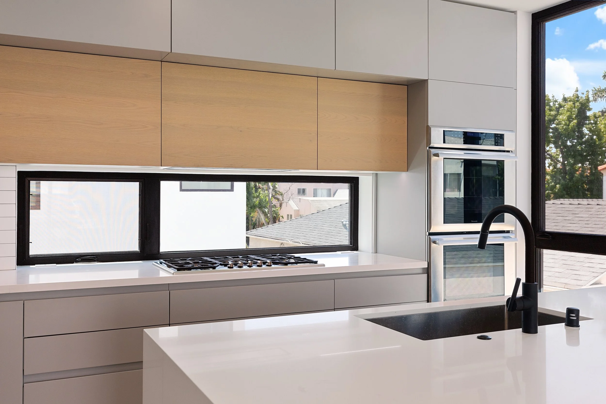 Contemporary kitchen featuring a waterfall quartz island, custom cabinetry, and expansive horizontal windows in a Faircrest Heights townhome.