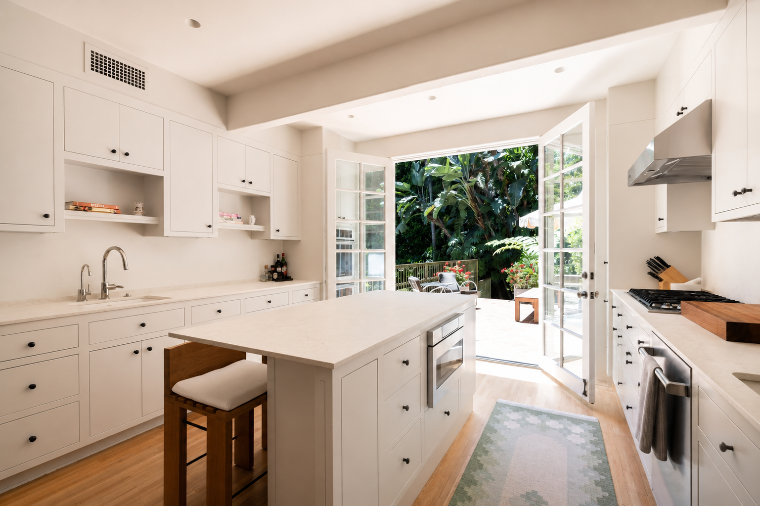Custom Spanish Revival kitchen renovation with white cabinetry, natural stone countertops, and French doors opening to the garden.