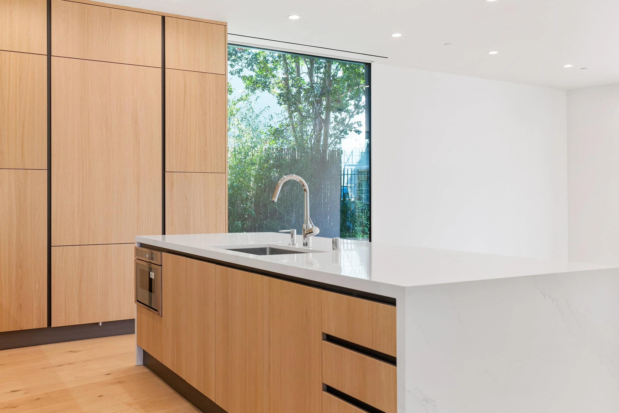 Bespoke kitchen with a waterfall quartz island, precision millwork, and oversized windows that bring natural light into the heart of the home, built by JBurton General Contractor.