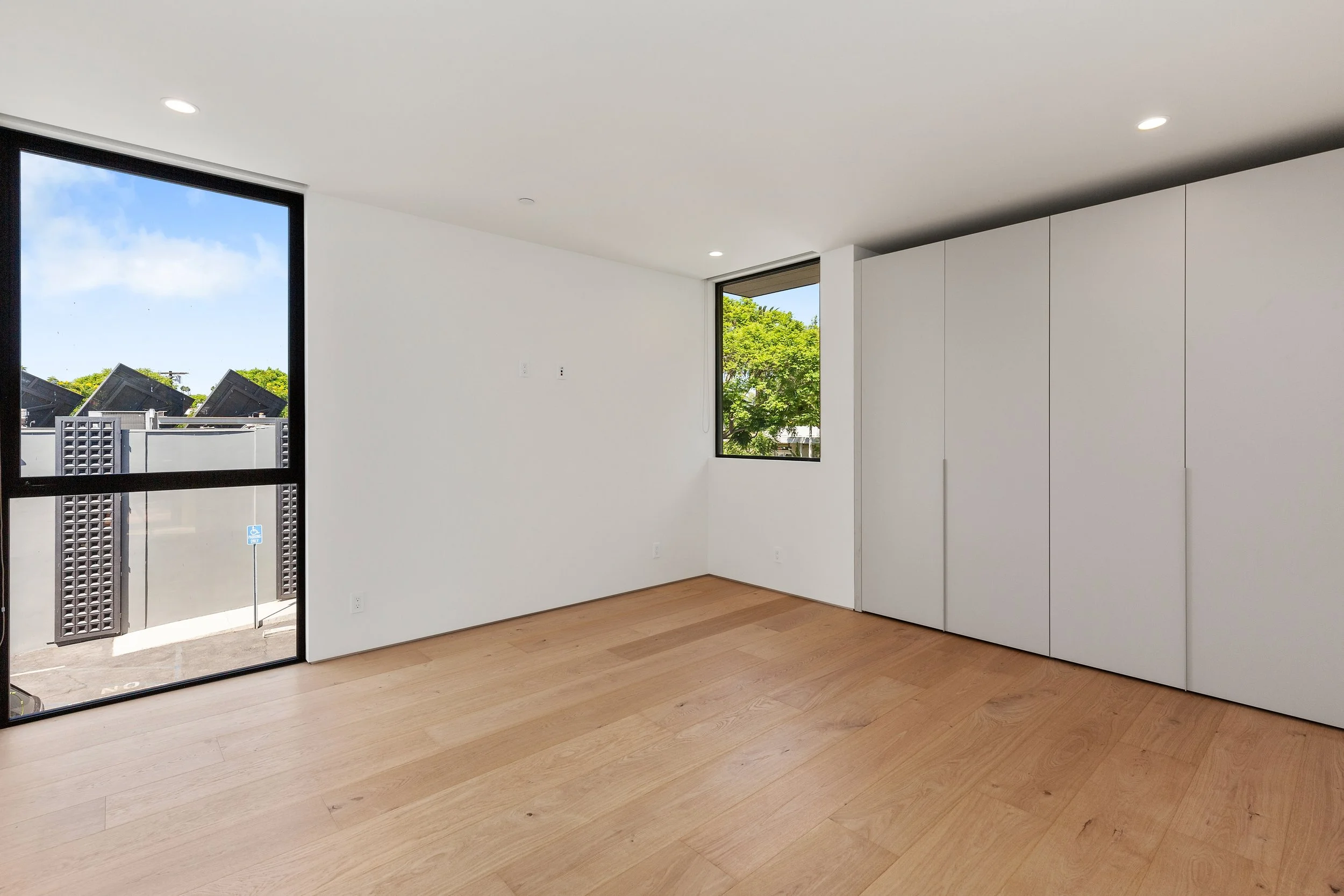 Versatile bedroom featuring wide-plank oak flooring, full-height custom closets, and expansive windows that maximize natural daylight, completed by JBurton General Contractor.