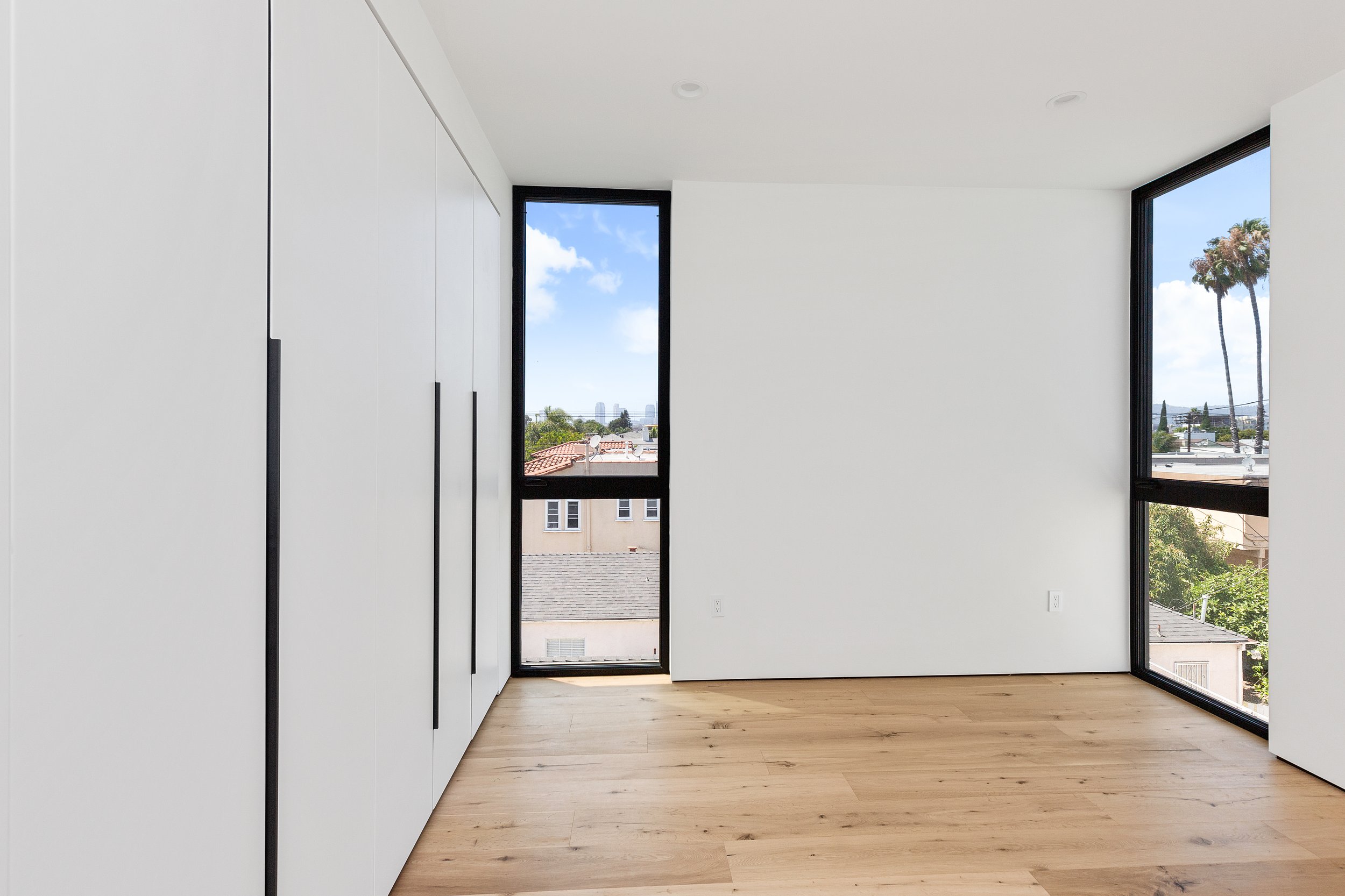 Bright bedroom with floor-to-ceiling window, custom wardrobe, and wide-plank oak flooring, completed by JBurton General Contractor in a Faircrest Heights townhome.