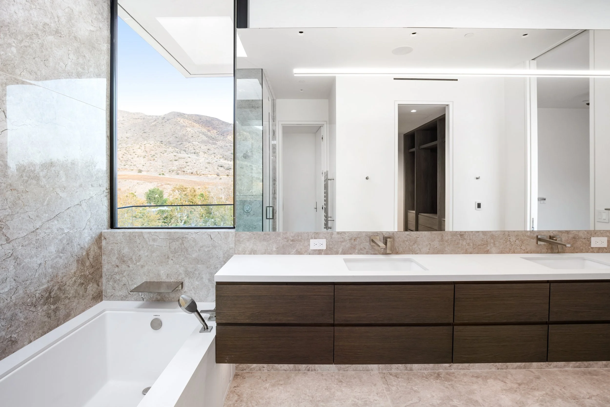 Primary bathroom with floating walnut vanity, natural stone finishes, and scenic Malibu views by JBurton General Contractor.