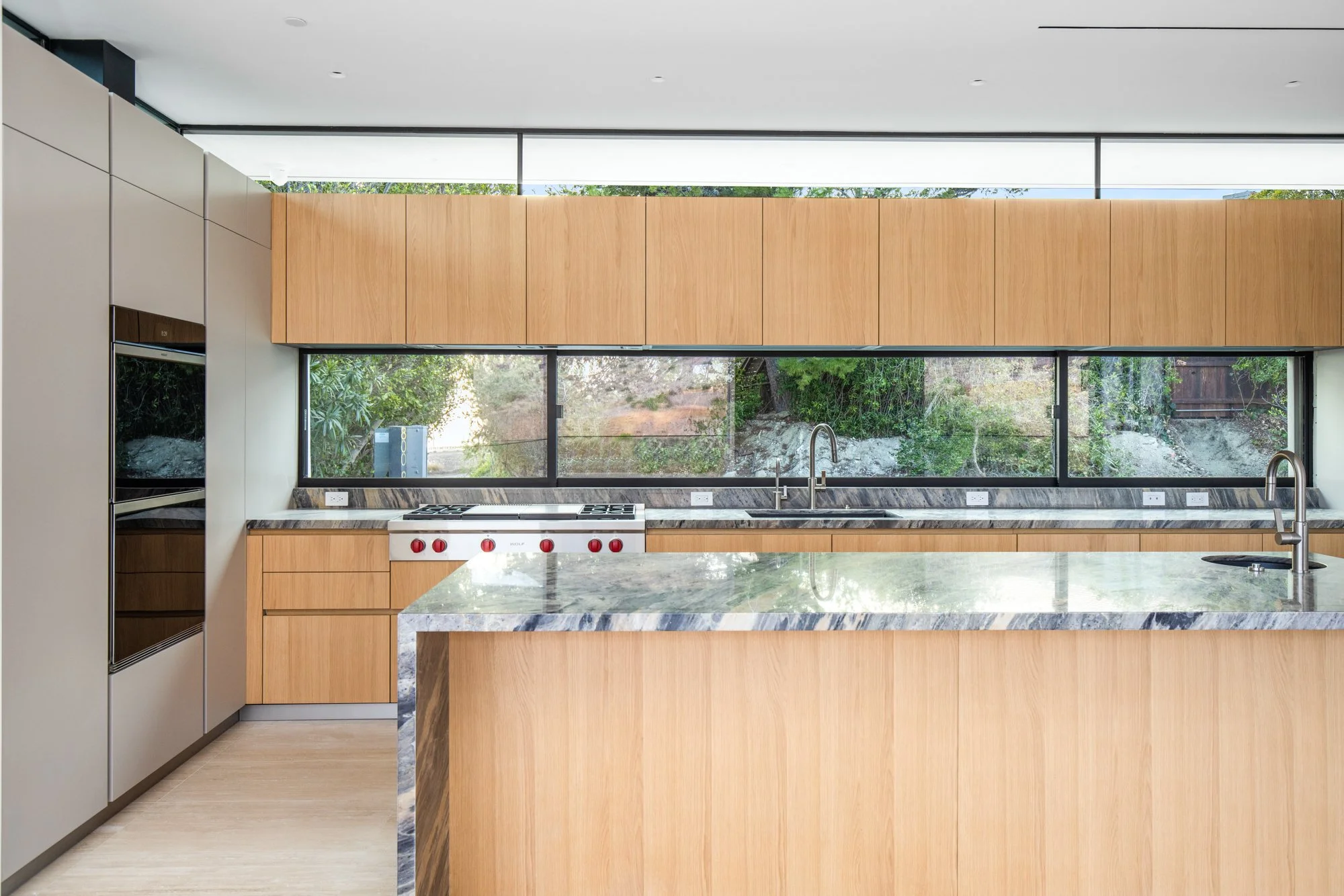 Custom white oak kitchen with panoramic windows, premium appliances, and natural stone countertops by JBurton General Contractor.