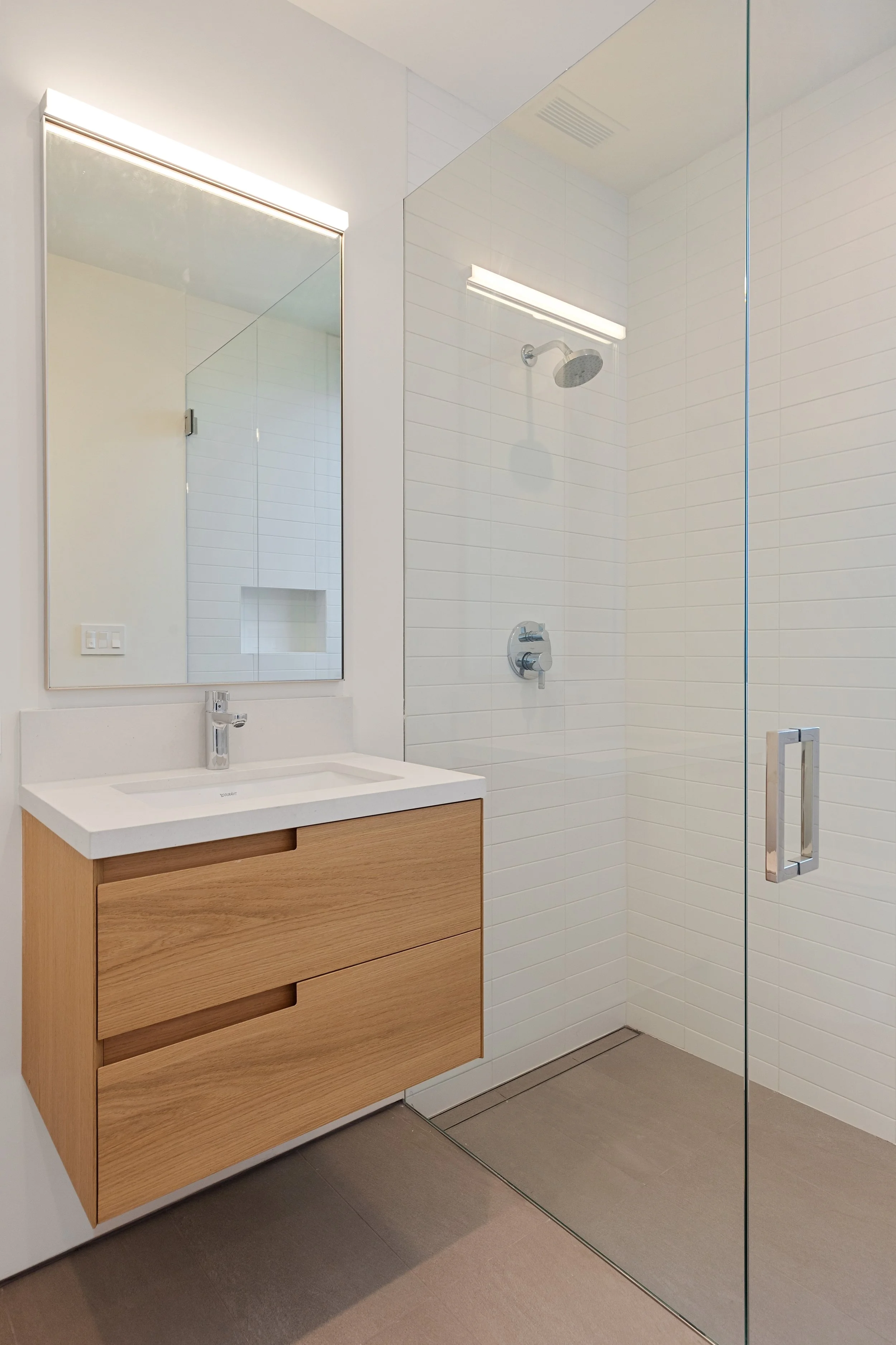 Guest bathroom with floating oak vanity, frameless glass shower, and streamlined contemporary finishes, constructed by JBurton General Contractor.