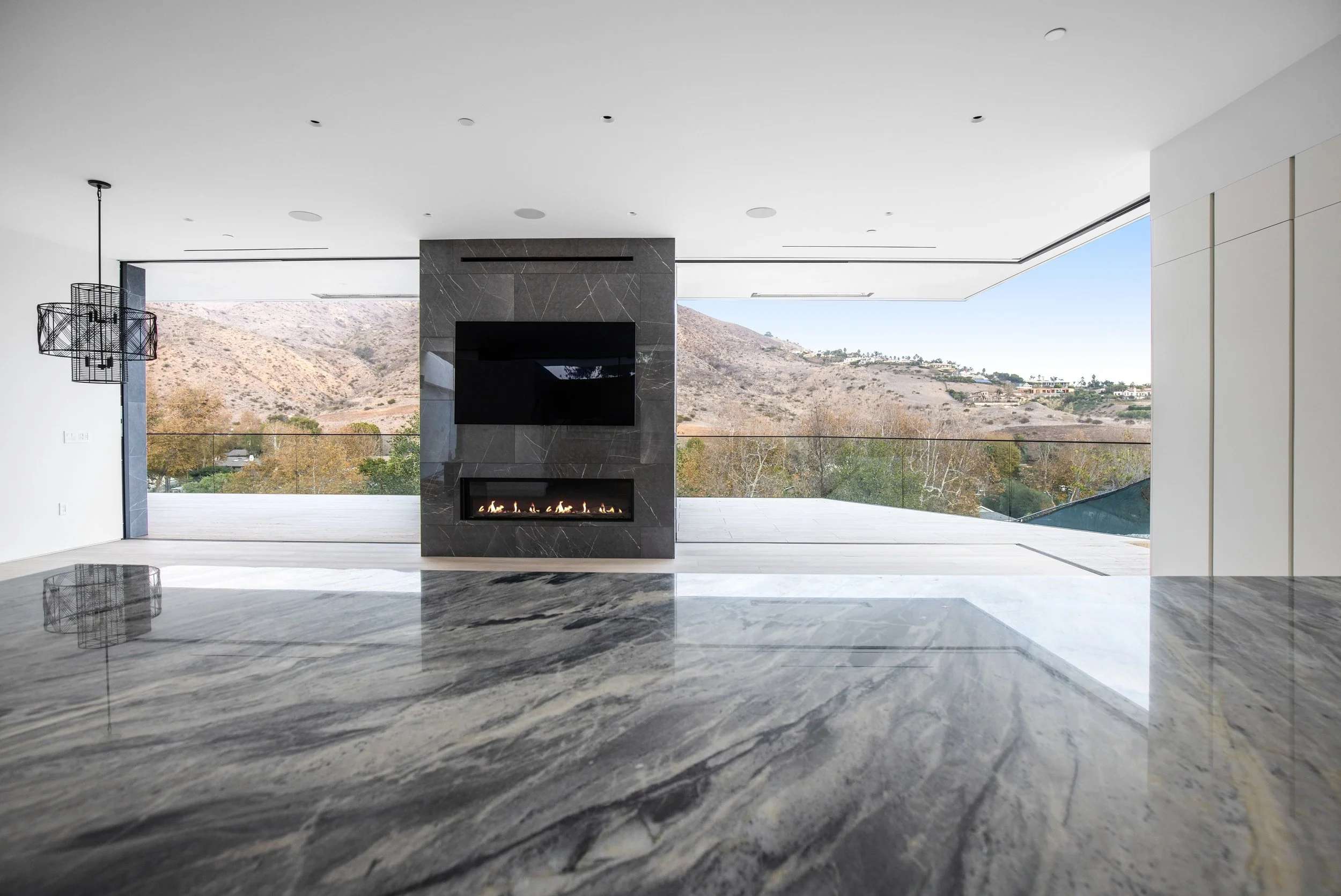 Indoor-outdoor living space featuring a modern fireplace, dramatic stone surfaces, and sweeping Malibu mountain views by JBurton General Contractor.