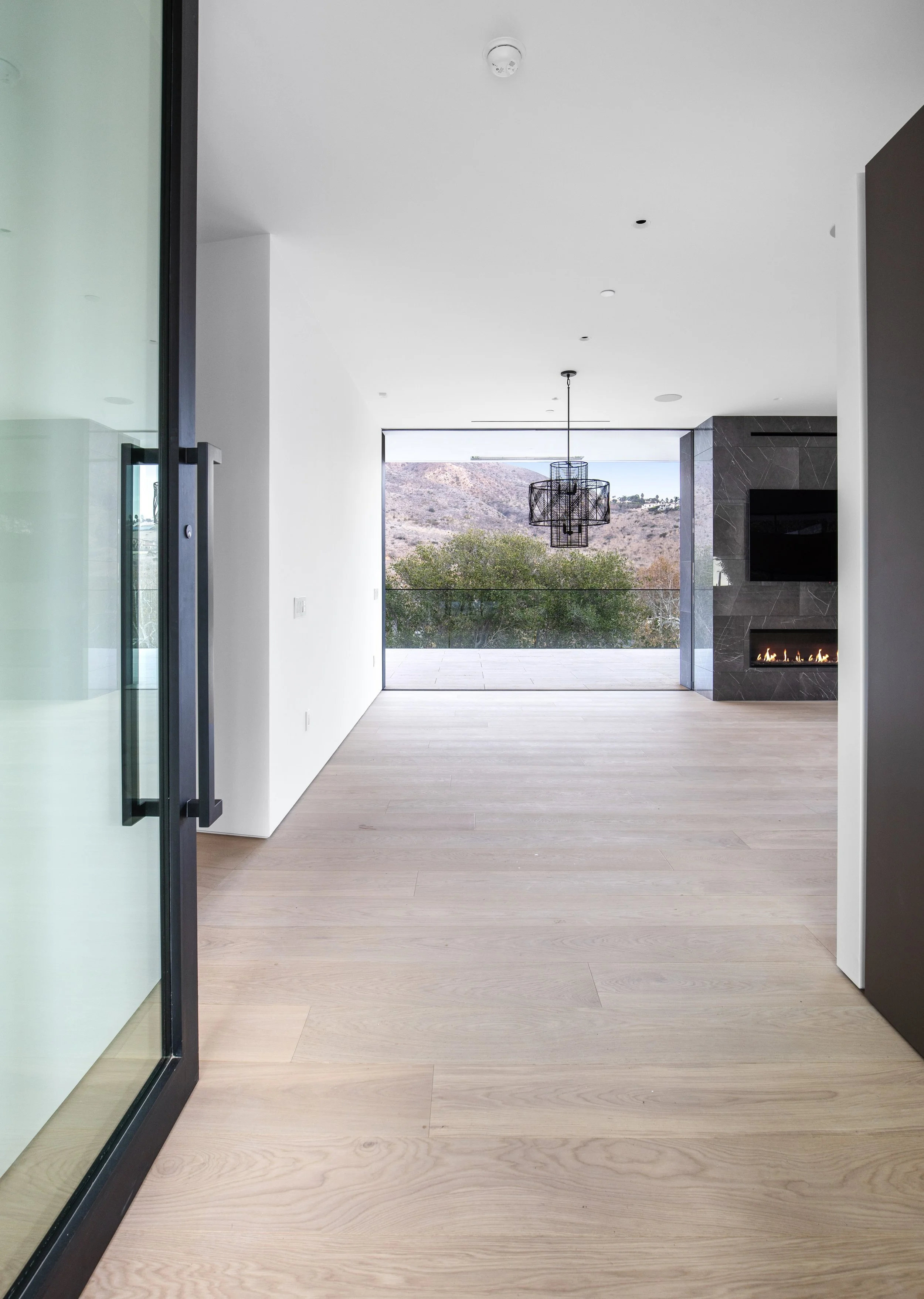 Seamless indoor-outdoor living with expansive glazing, a sculptural fireplace, and panoramic mountain views in a Malibu custom home by JBurton General Contractor.