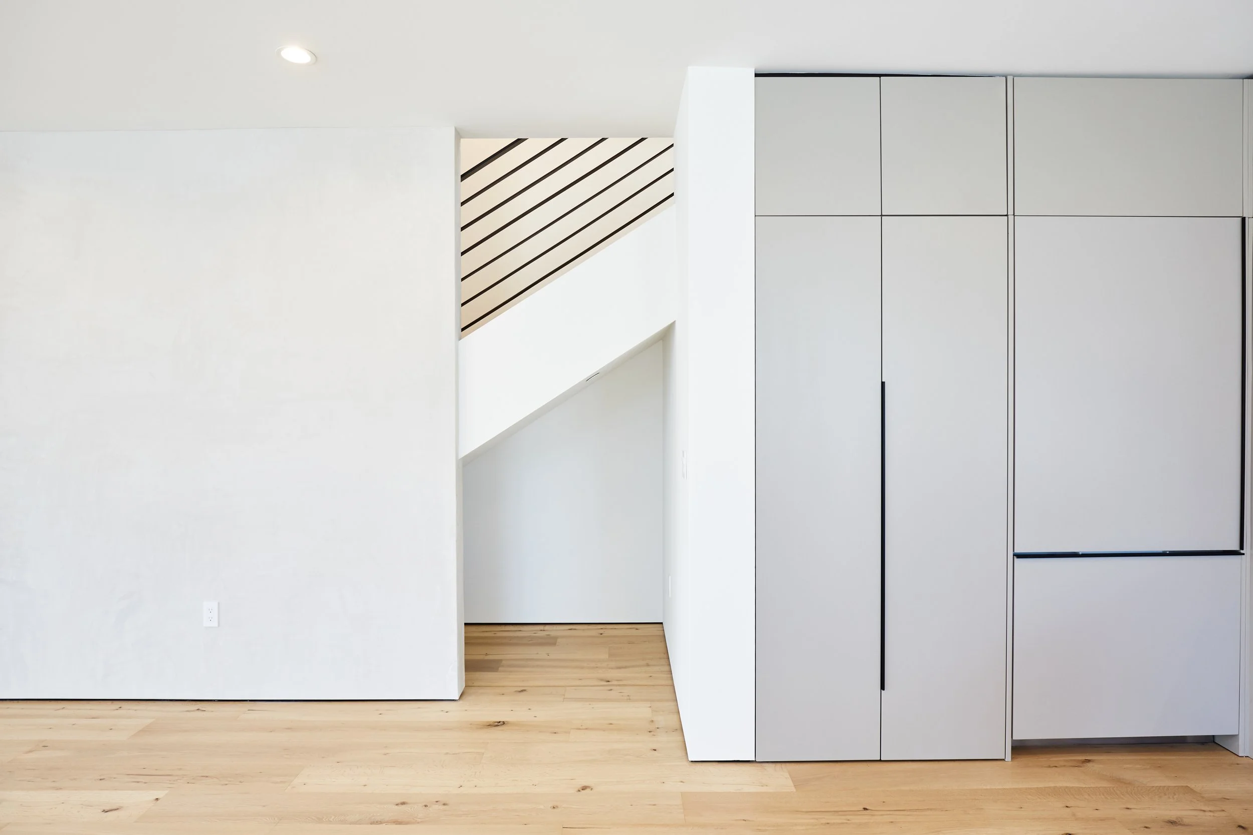 Contemporary staircase with custom built-in storage and wide-plank hardwood flooring in a Los Angeles townhome