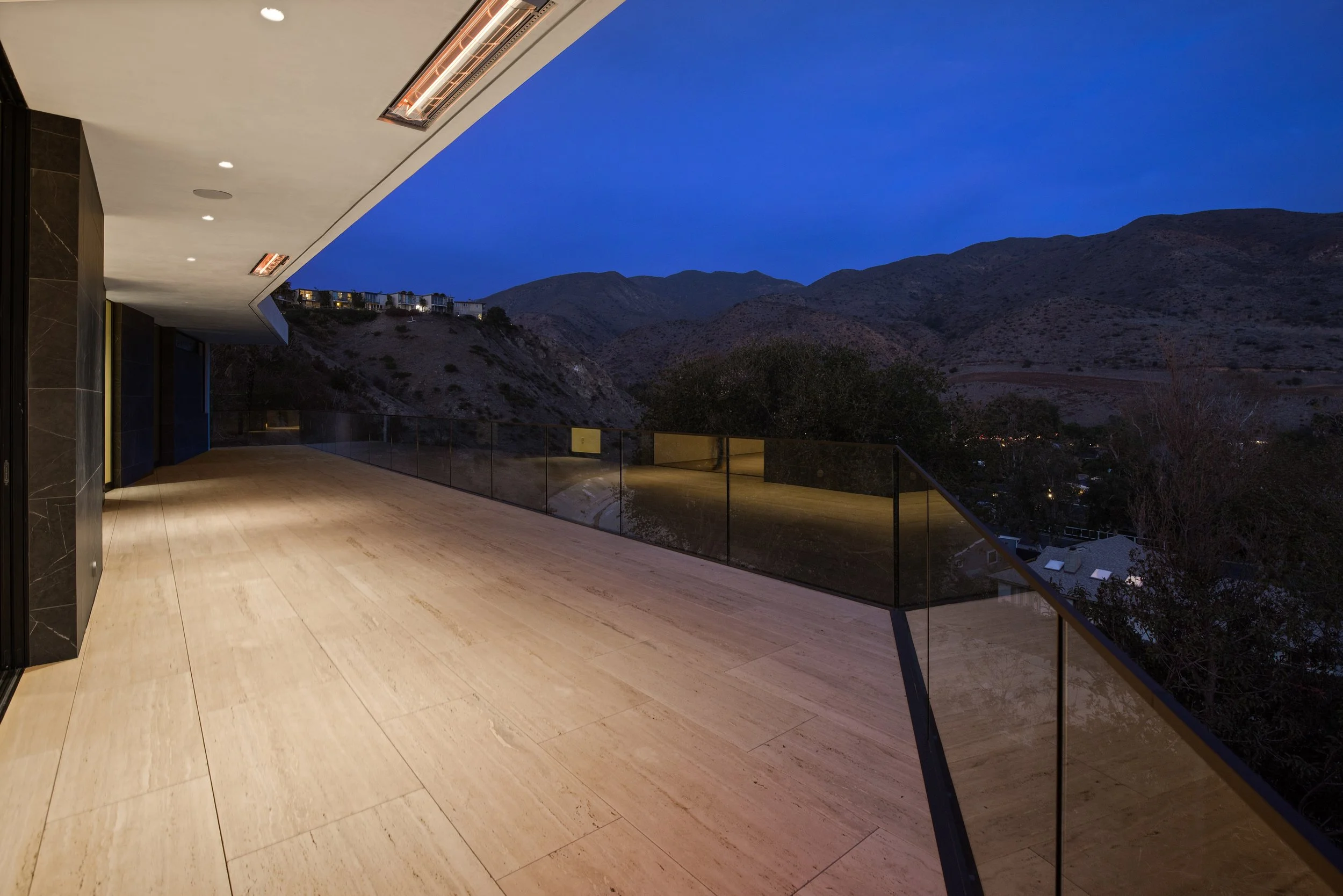 Covered outdoor terrace with architectural lighting, porcelain flooring, and unobstructed mountain views in a custom Malibu home by JBurton General Contractor.