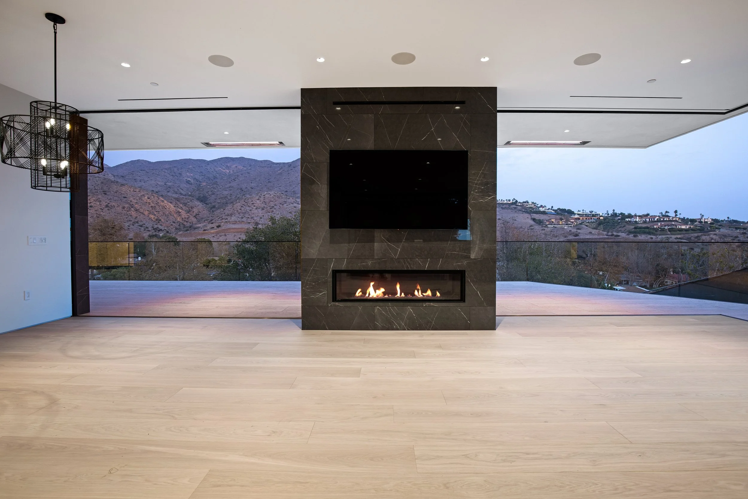 Statement fireplace feature wall anchoring an open-concept great room with floor-to-ceiling glazing and breathtaking Malibu views, constructed by JBurton General Contractor.