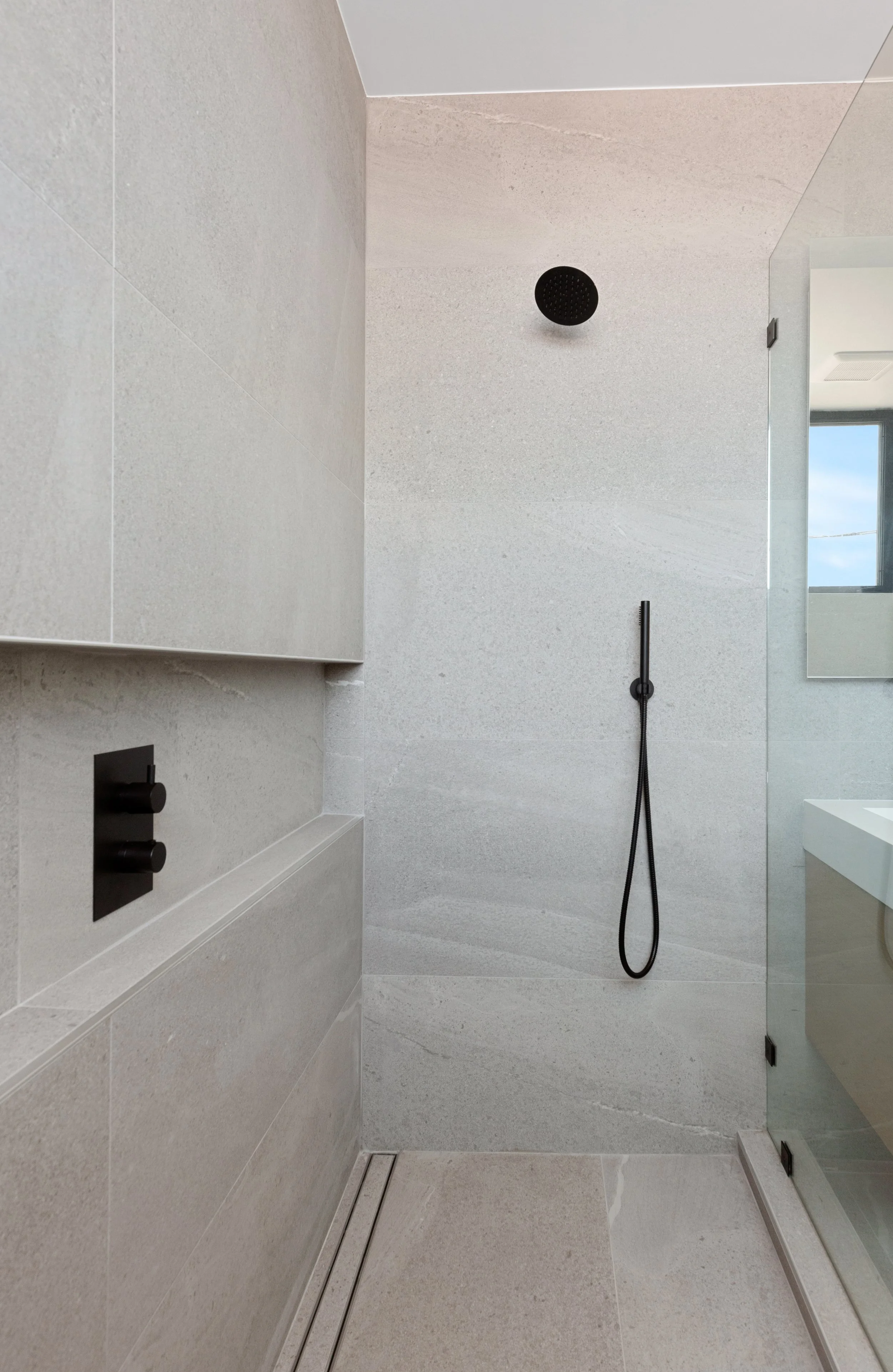 Modern walk-in shower with large-format tile, frameless glass enclosure, and matte black plumbing fixtures in a Faircrest Heights townhome.