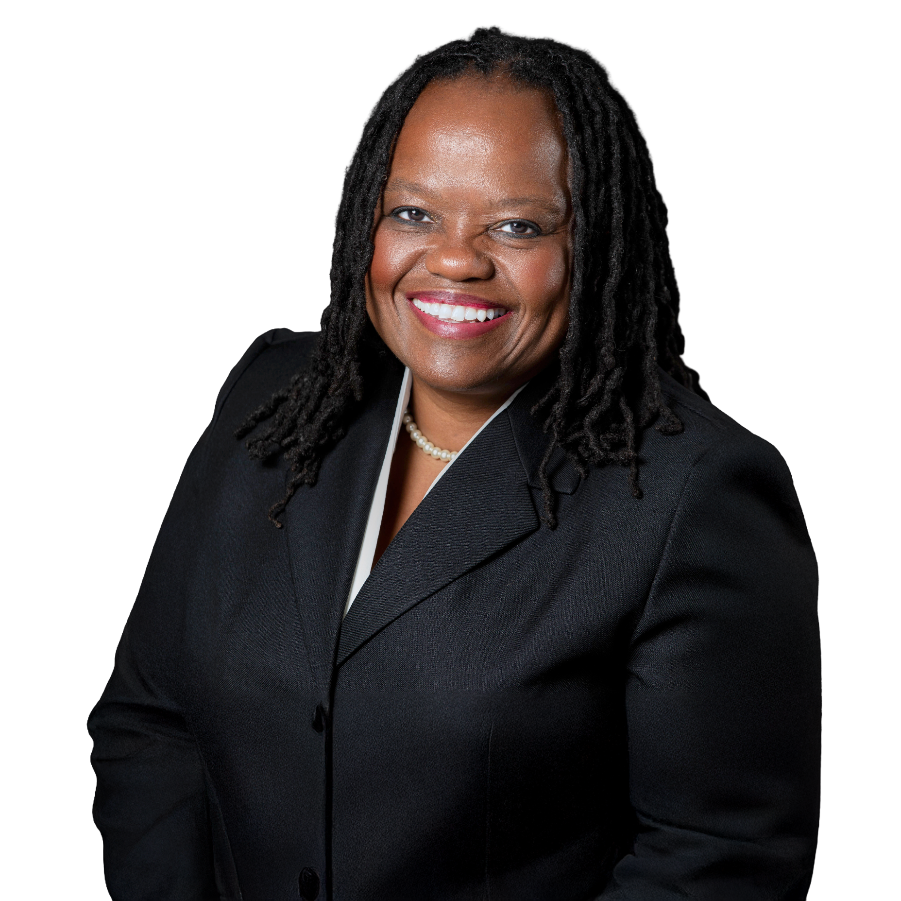 A professional woman with shoulder-length black dreadlocks, wearing a black blazer and a pearl necklace, smiling at the camera against a black background.