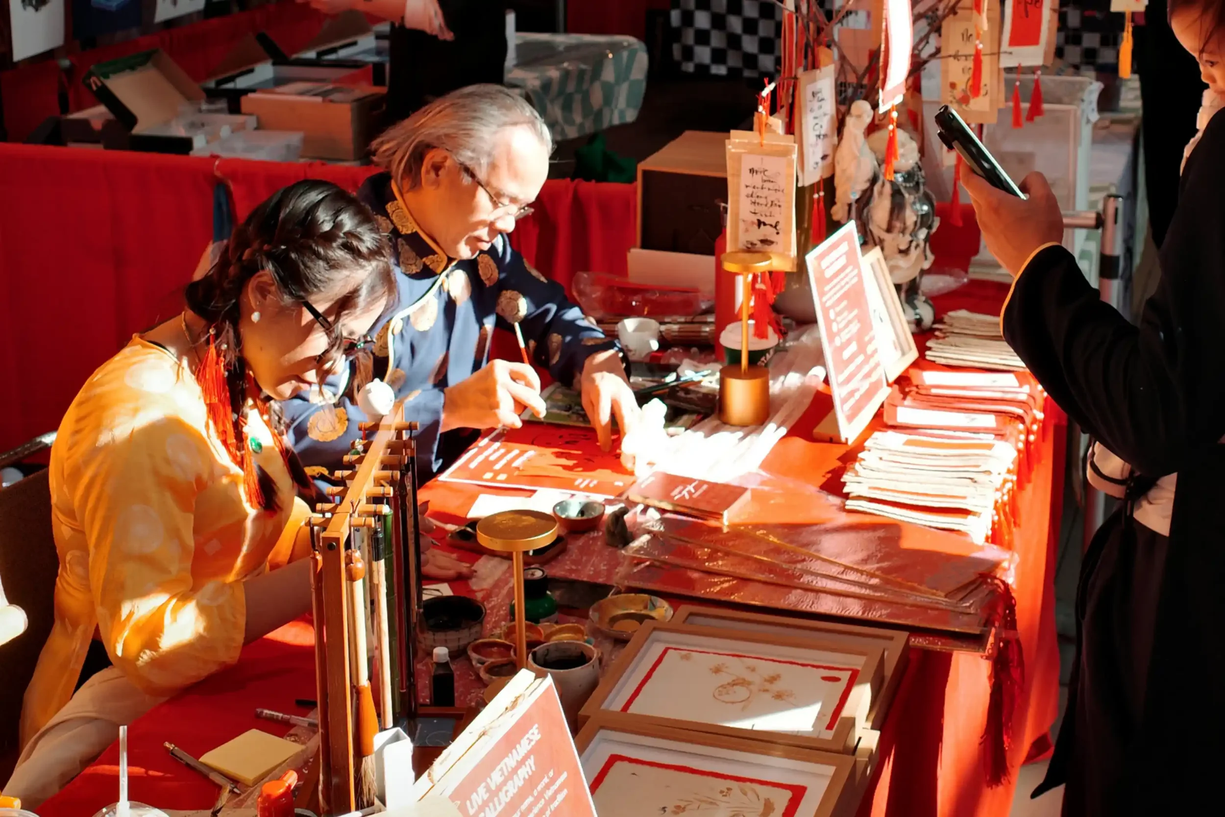 Linh Nguyen and her father doing live Vietnamese calligraphy together at Tết in Seattle 2025, surrounded by ink, brushes, and red paper under warm golden light.