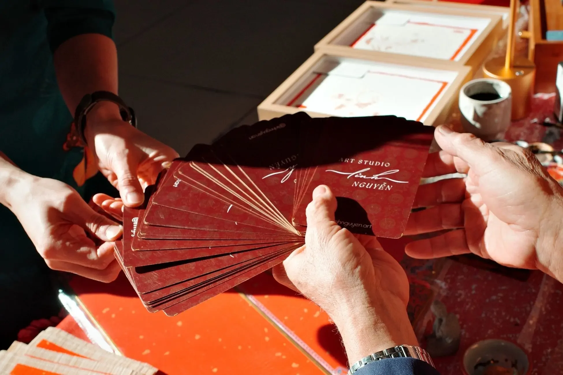 A customer drawing from Linh Nguyen's prosperity word card deck at Tết Seattle 2025, with 45 handcrafted Vietnamese calligraphy cards fanned out between two pairs of hands.