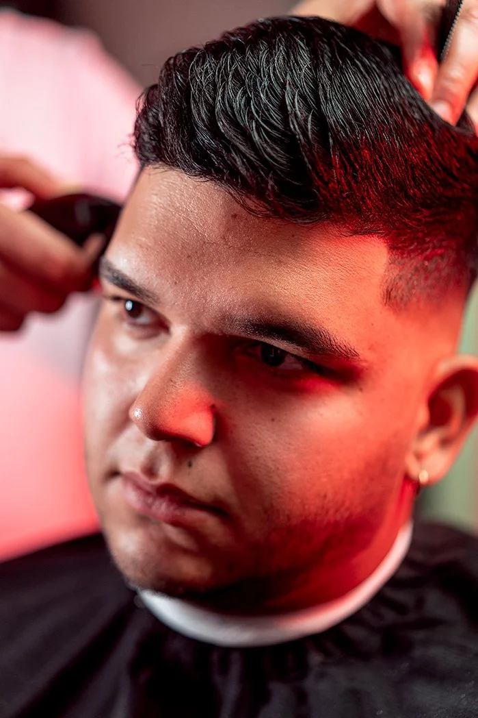 Close-up of a man getting a haircut, with red lighting illuminating his hair and face.