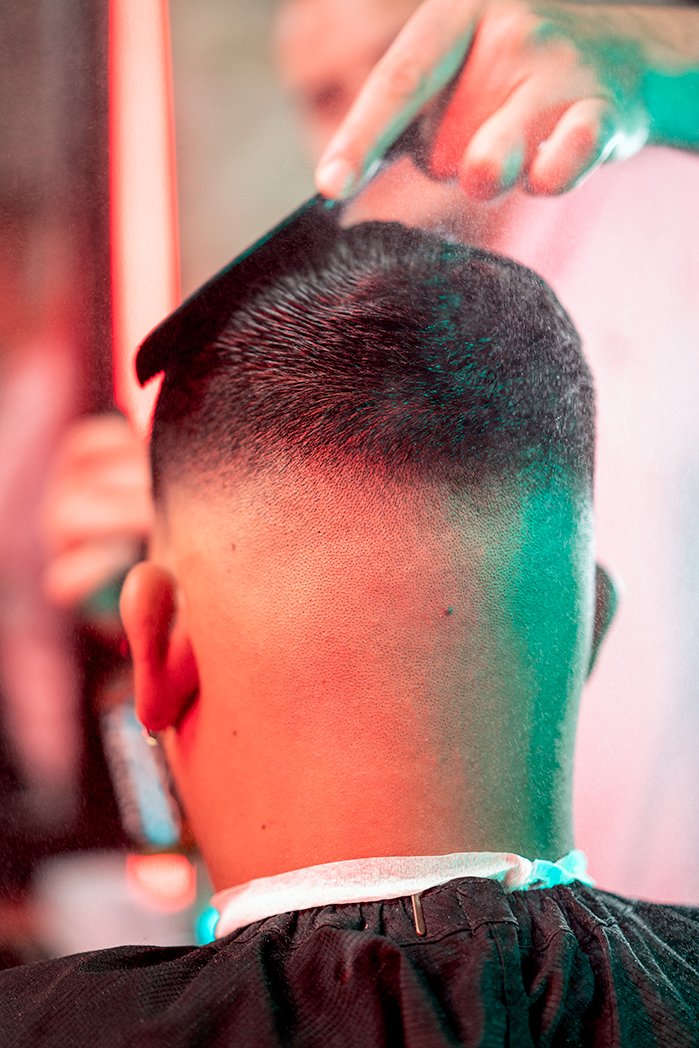 A person getting a short, faded haircut in a barbershop, with the barber using clippers to trim the hair.