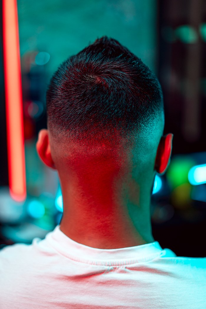 Back of a person's head with a fresh fade haircut, illuminated by colorful neon lights.