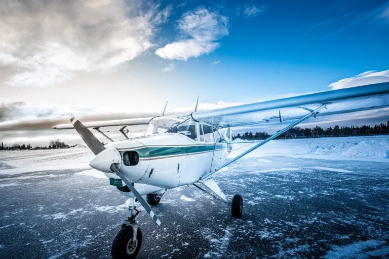 Small white airplane on a snow-covered tarmac with a cloudy sky.