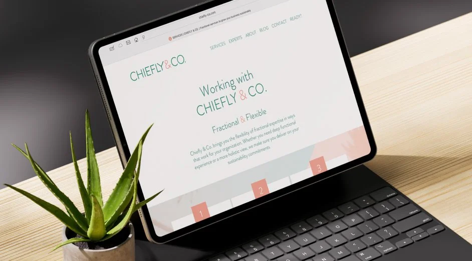 A tablet on a desktop displaying a webpage for CHIEFLY & CO, with a phrase about working with them and a menu bar, placed next to a potted aloe vera plant on a light-colored wooden surface.