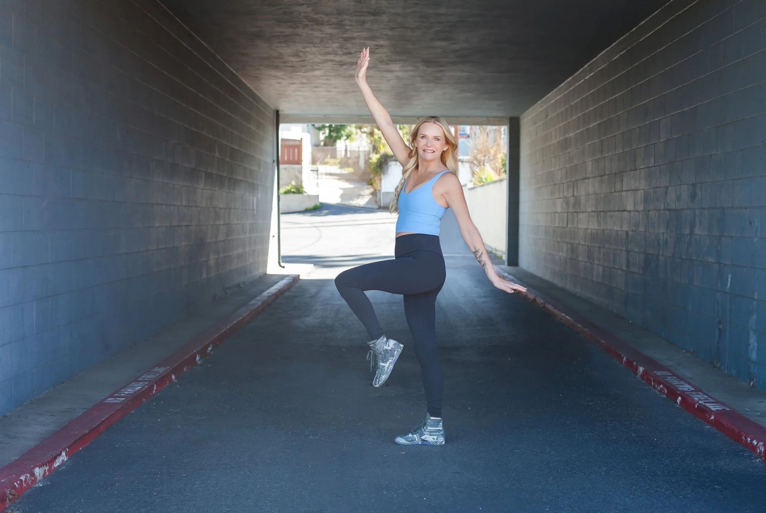 Woman in athletic clothes performing a dance or pose under an underpass.